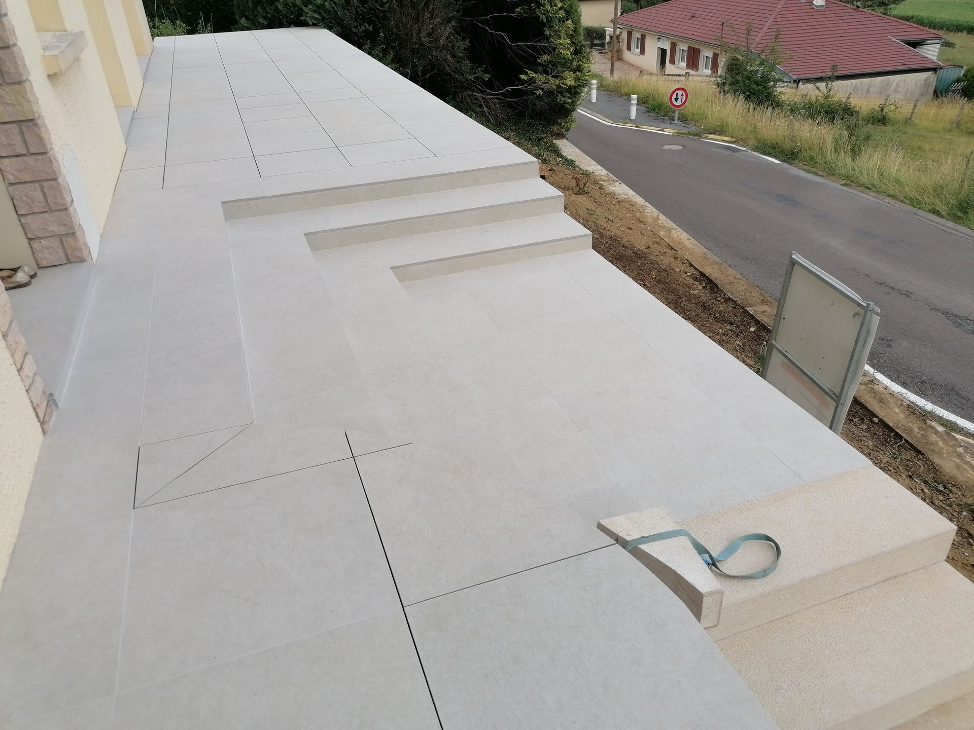 Une terrasse en béton gris clair en construction, avec escalier intégré, donnant sur une route et un paysage rural.
