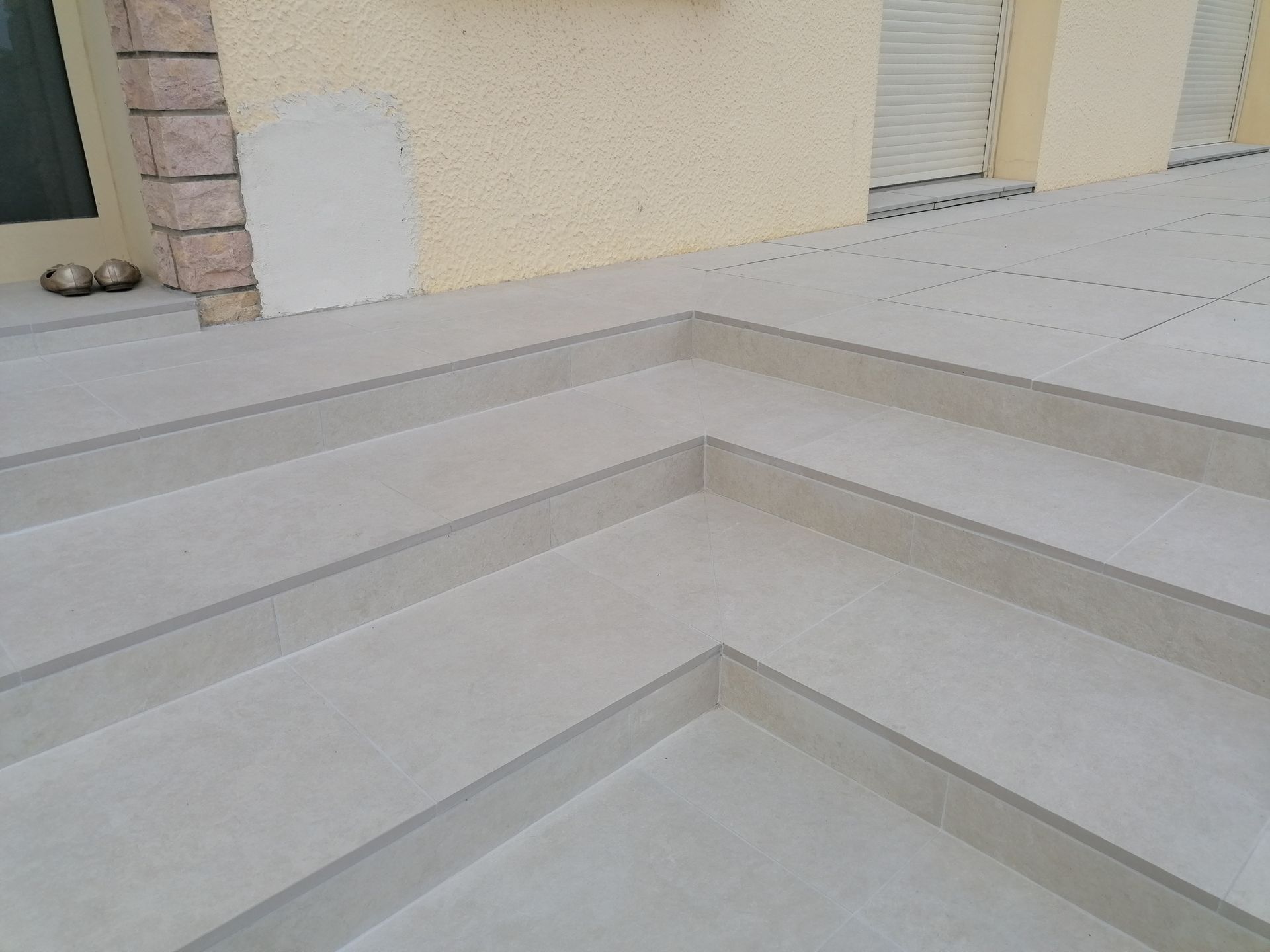 Vue d'angle d'un escalier extérieur en pierre gris clair menant à une maison au mur beige texturé.