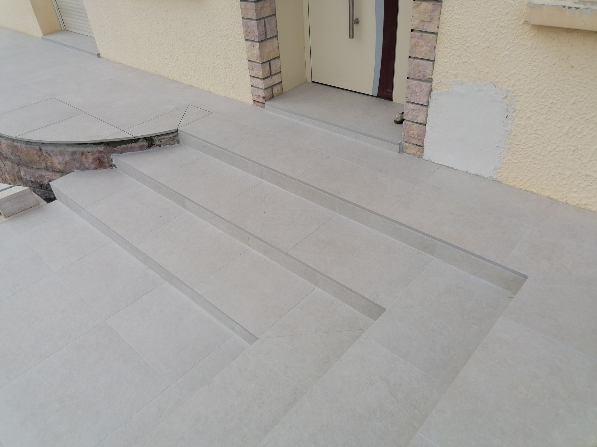 Deux marches en béton mènent à l'entrée principale d'un bâtiment aux murs clairs et aux détails d'encadrement de porte en pierre.