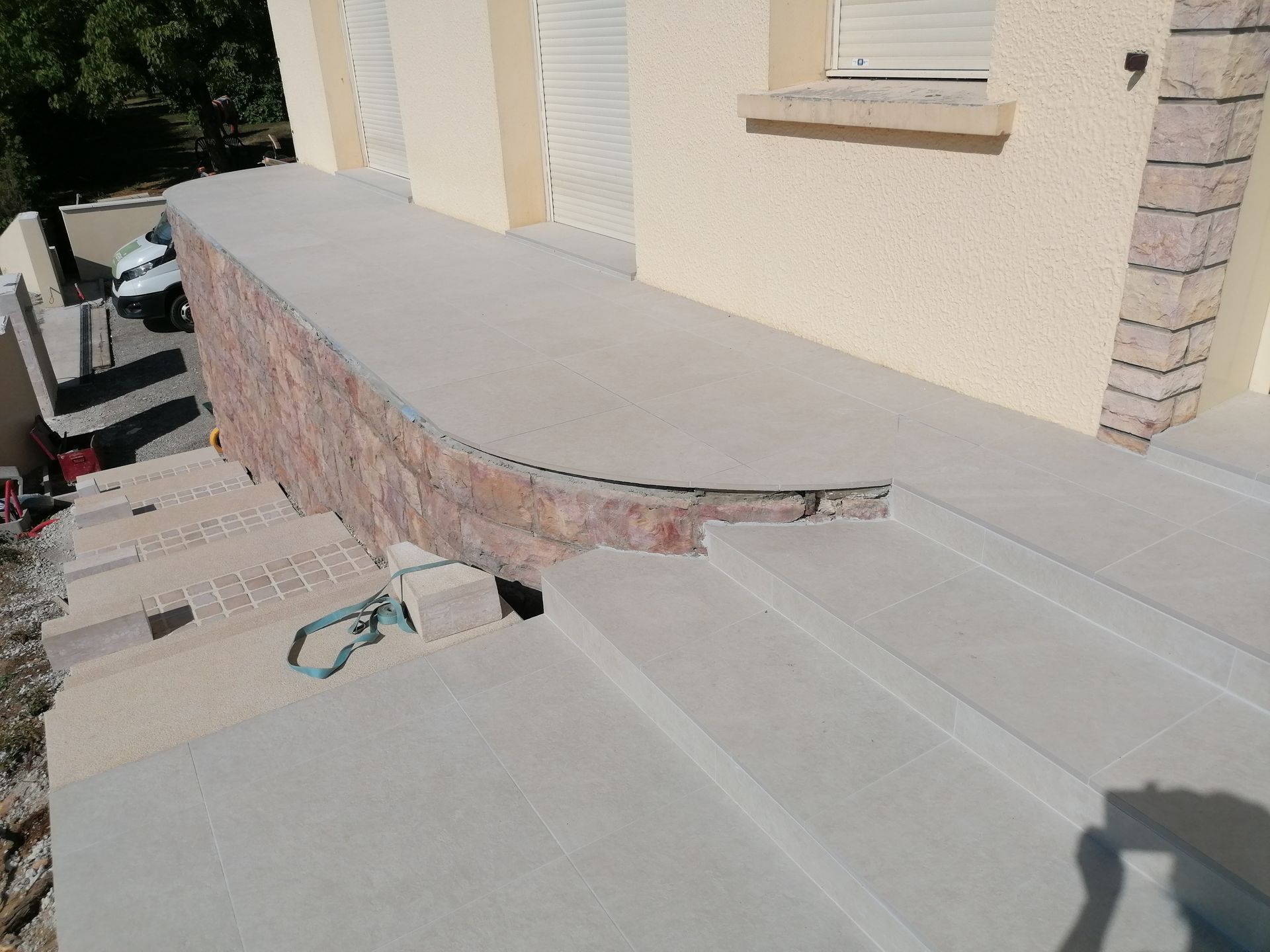 Mur en pierre à sommet arrondi et escalier menant à l'étage. Bardage beige et stores fermés visibles.