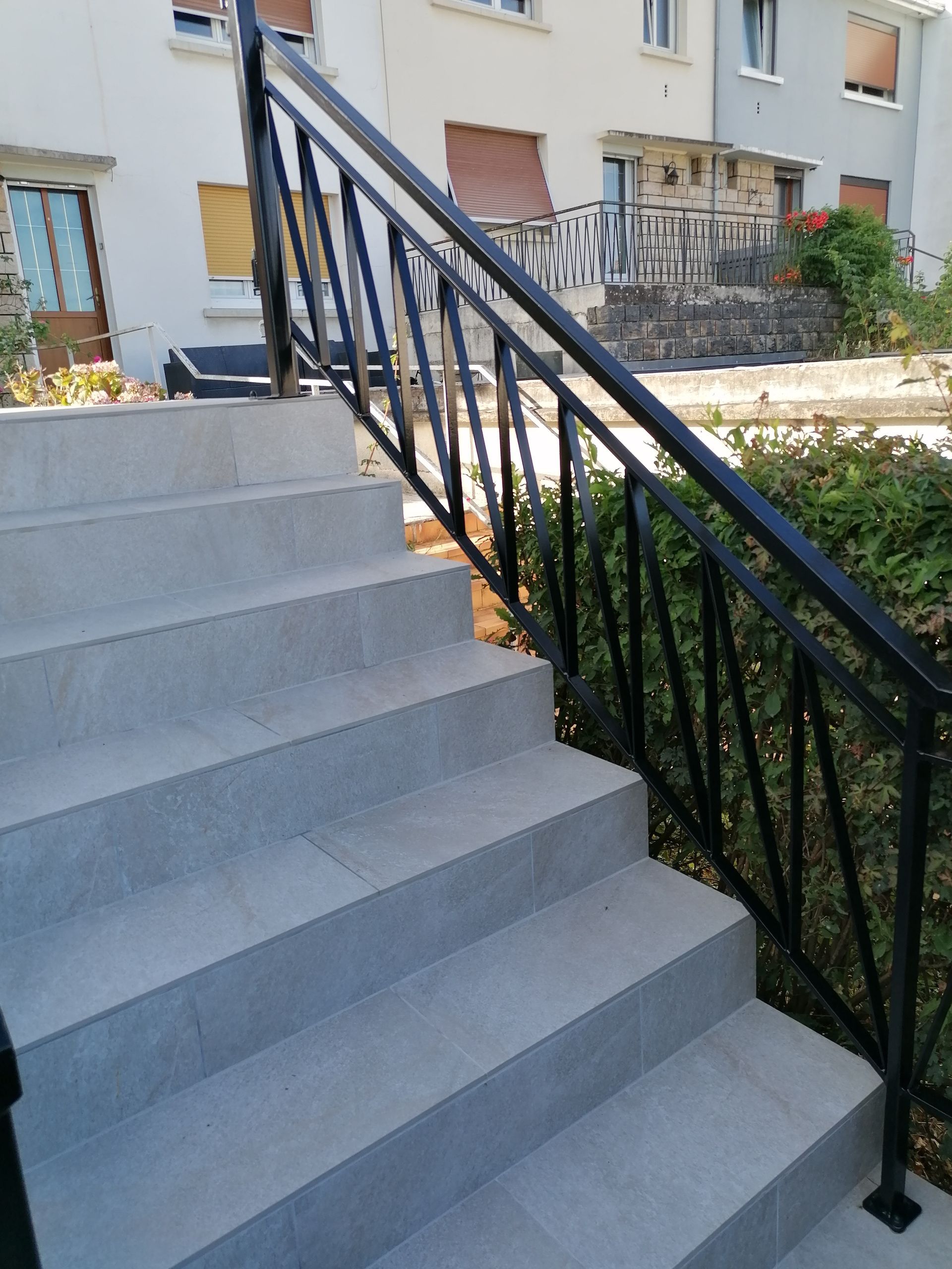 Un escalier extérieur en pierre avec une rampe en métal noir, menant à des bâtiments résidentiels.