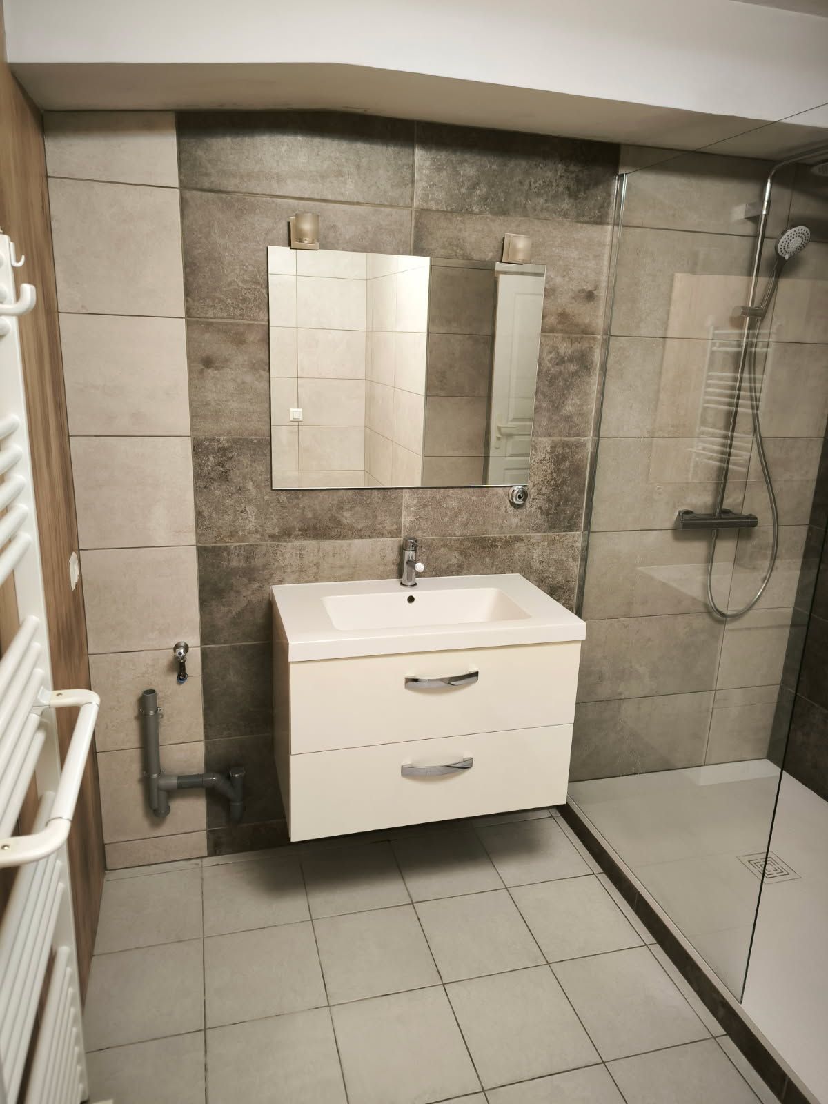 Une salle de bains moderne avec un meuble-lavabo suspendu blanc, un miroir rectangulaire et une douche à l'italienne aux murs carrelés de gris.