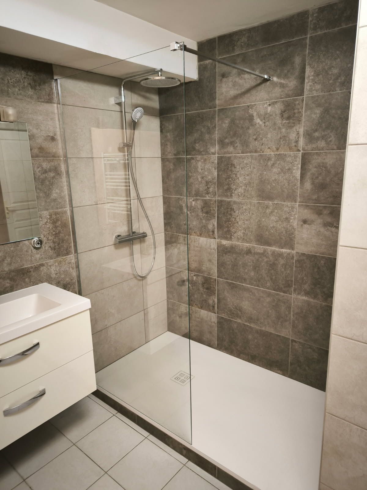 Salle de bains moderne avec douche à l'italienne dotée d'une paroi en verre, carrelage mural imitation pierre foncée et meuble-lavabo blanc.