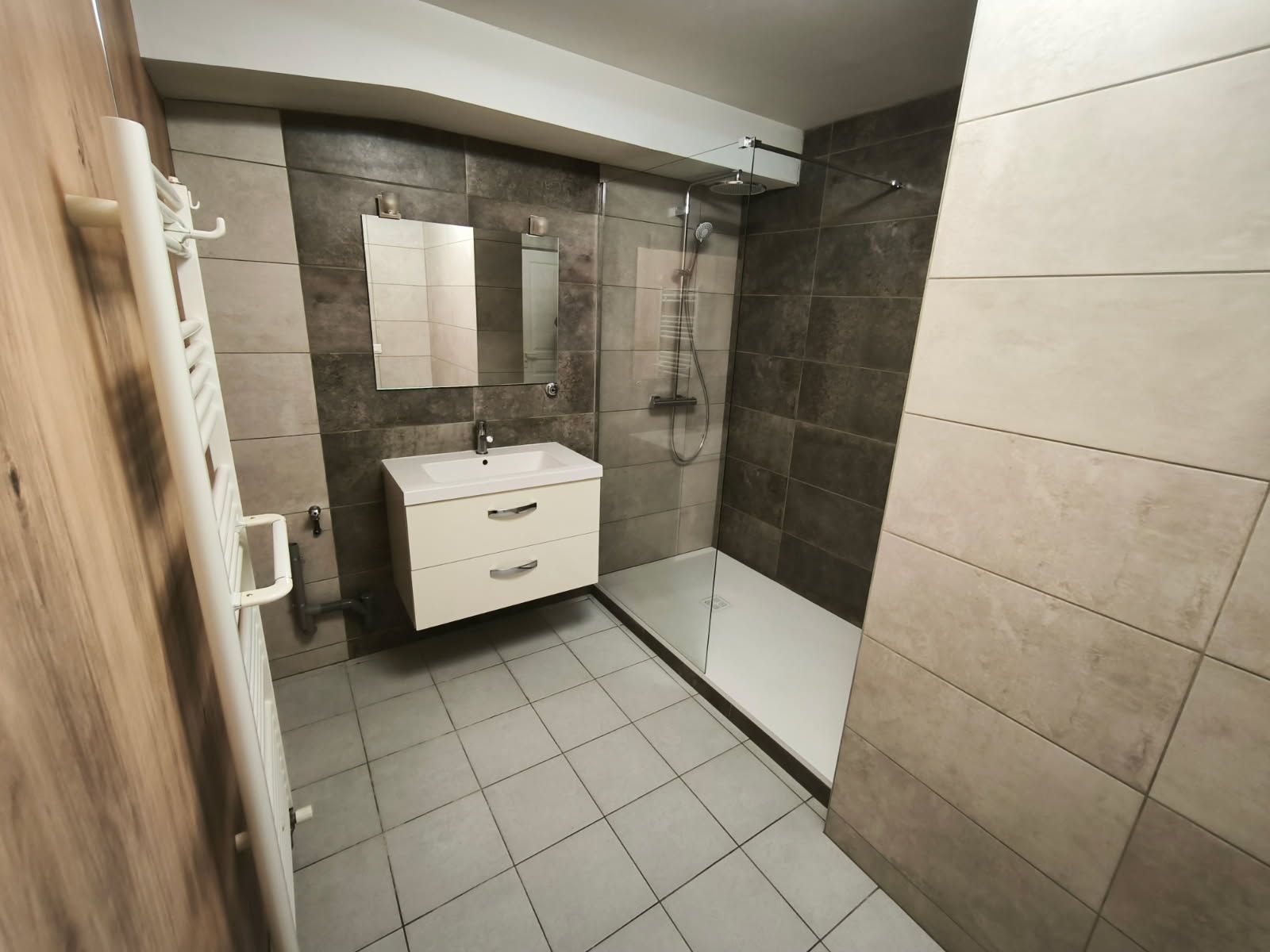 Salle de bains moderne avec carrelage au sol gris clair, carrelage mural beige, meuble-lavabo suspendu blanc et douche à l'italienne.