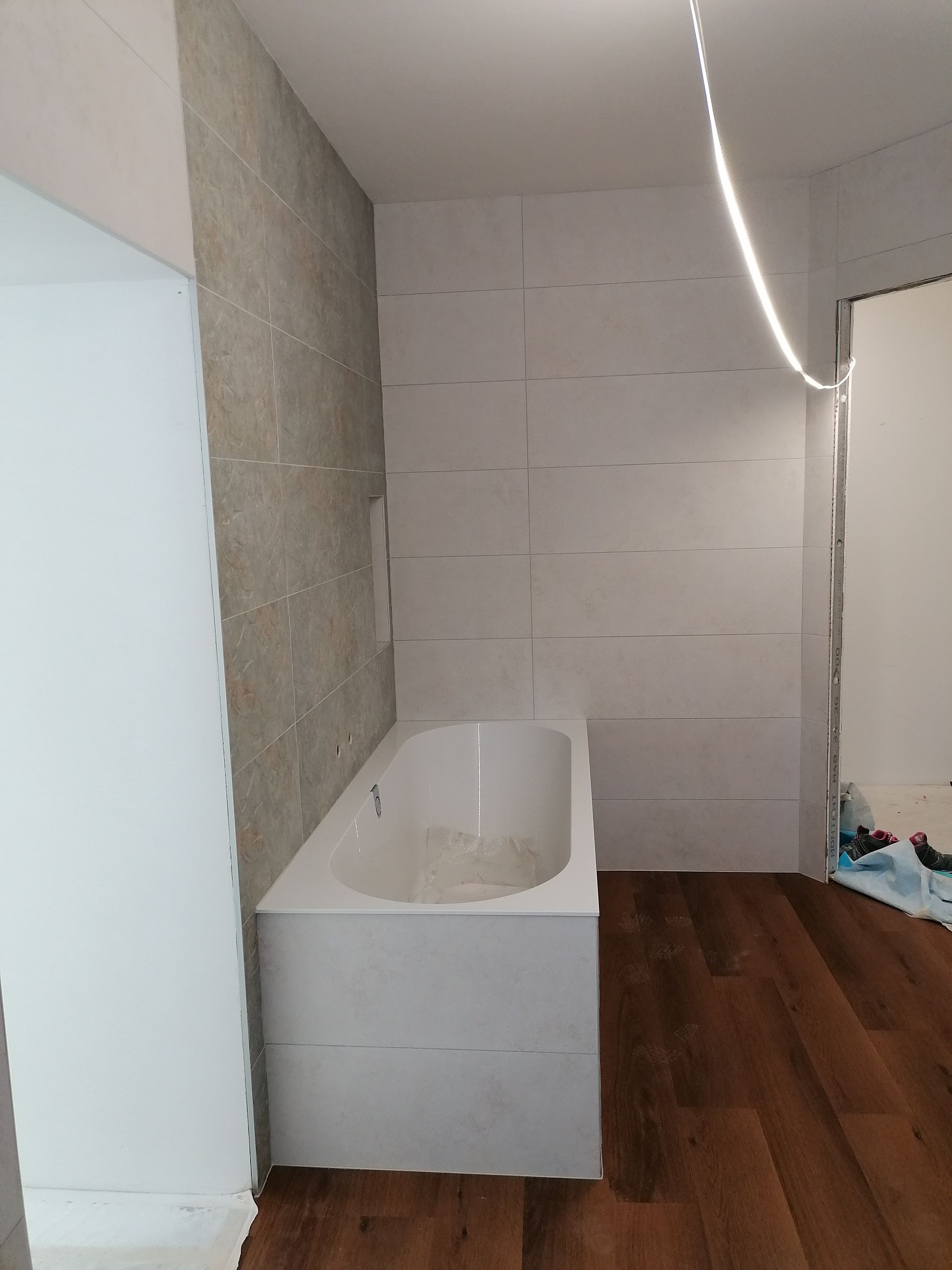 Une baignoire installée contre des murs lambrissés blancs dans une pièce au sol imitation bois foncé et aux éléments de construction apparents.