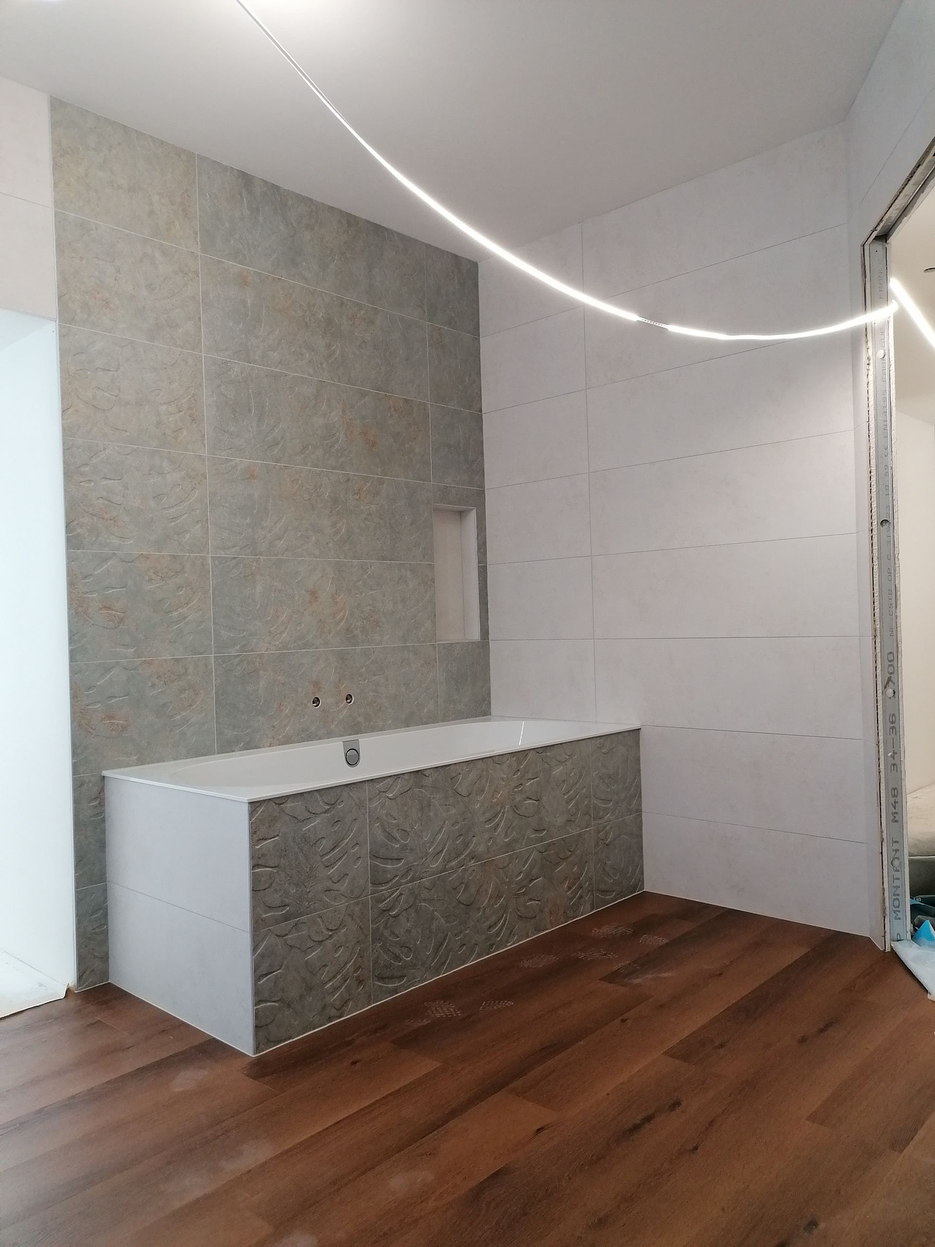 Salle de bains avec carrelage imitation marbre foncé, receveur de douche blanc et fenêtre.