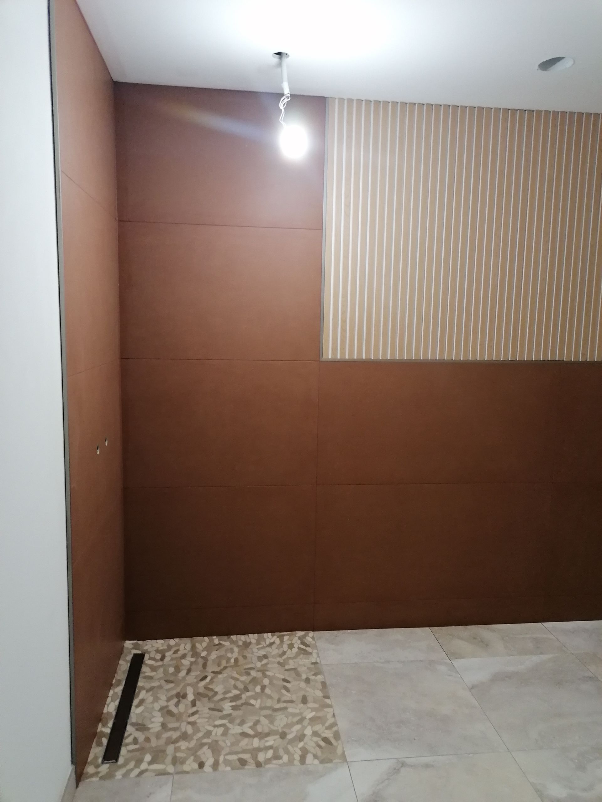 Un coin de pièce intérieure inachevé, avec des lambris bruns, un morceau de papier peint à rayures et un sol carrelé.