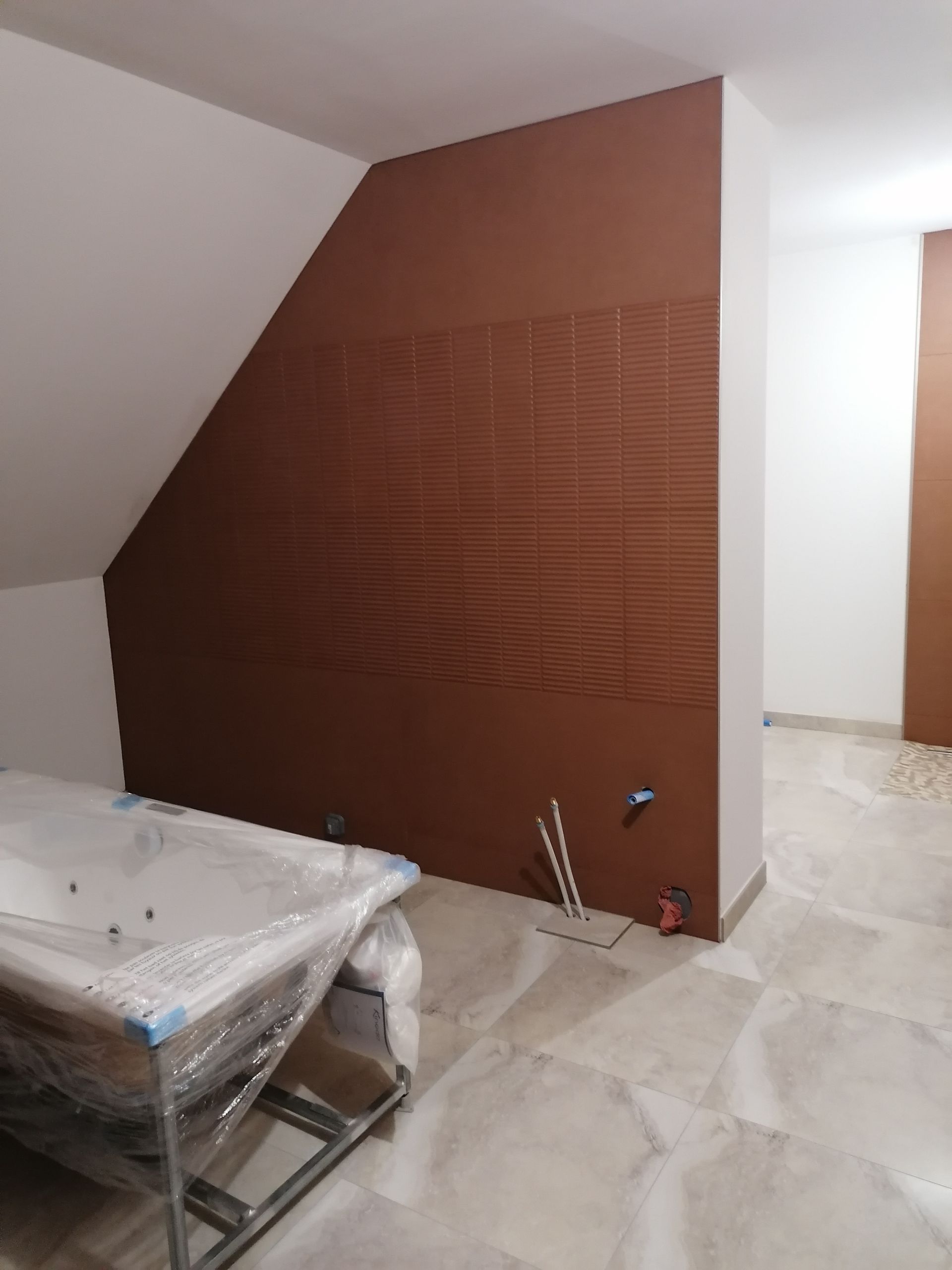 Une salle de bains en construction avec un mur texturé marron, une baignoire blanche recouverte de plastique et des carreaux de sol clairs.