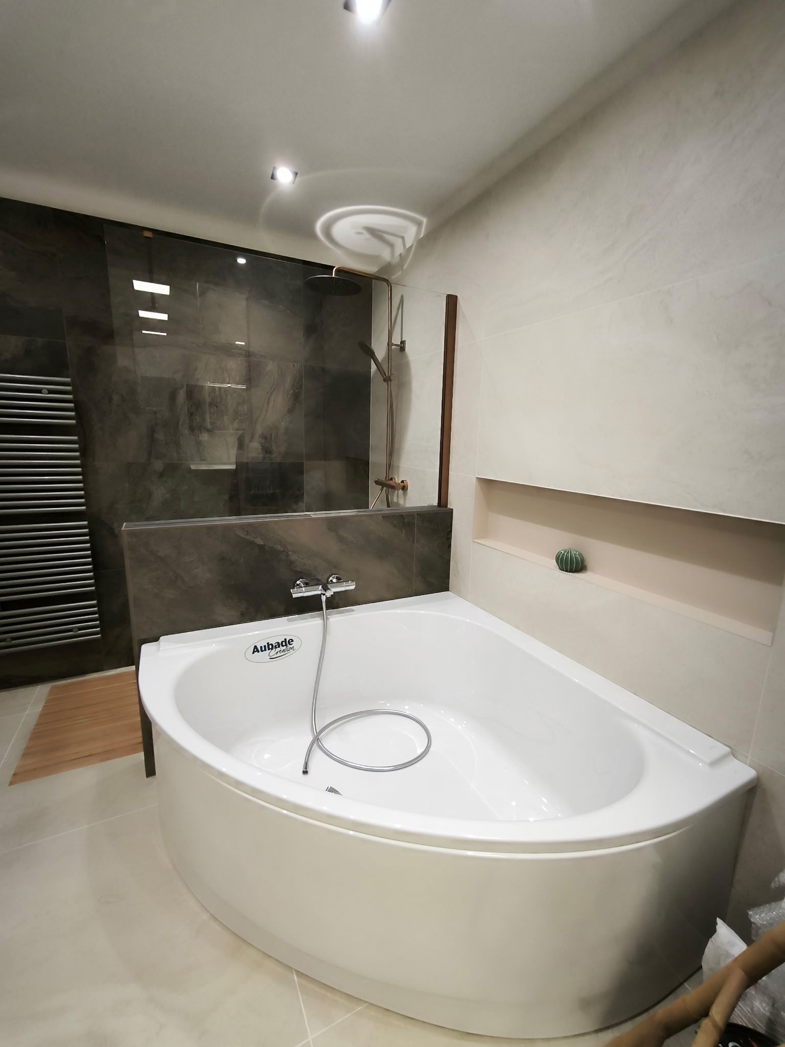 Une salle de bains moderne avec une baignoire blanche de forme ovale placée contre un mur carrelé foncé et un mur beige clair.
