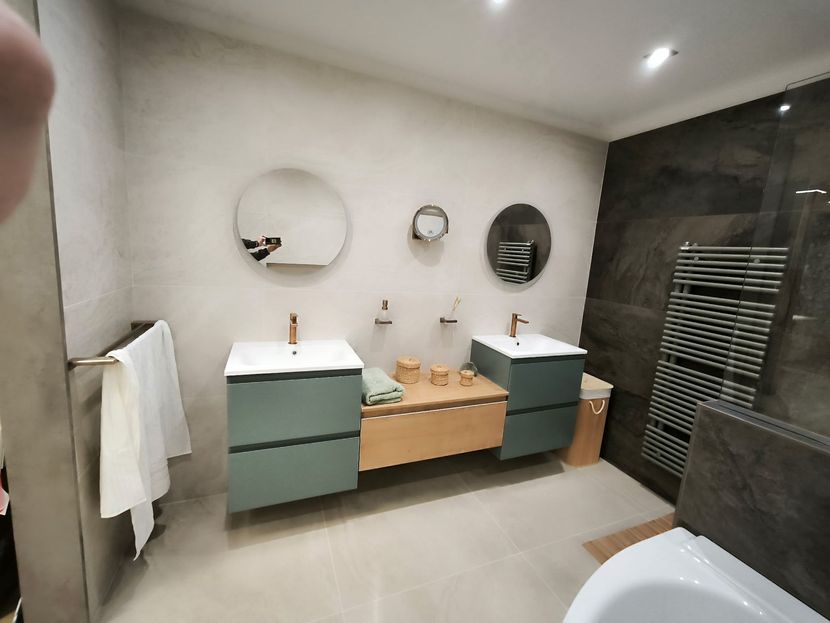Salle de bains avec deux lavabos, miroirs ronds, armoires vertes et sèche-serviettes chauffant.