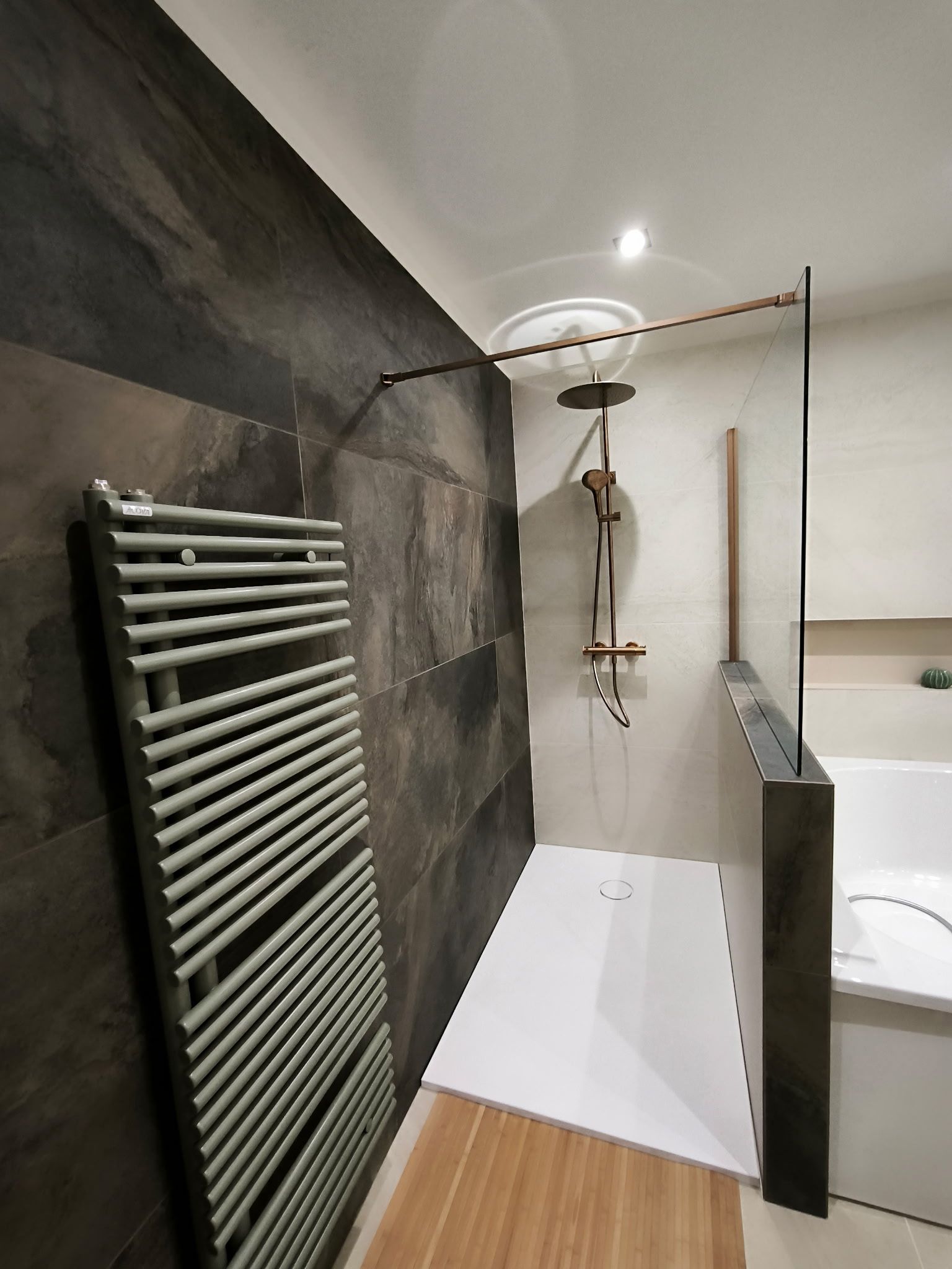 Salle de bains moderne avec un mur carrelé foncé, un sèche-serviettes gris, une douche à l'italienne blanche et une paroi en verre.