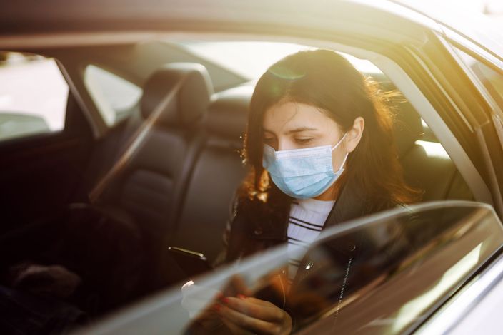 Photo d'une femme assise à l'arrière d'un taxi et portant un masque médical