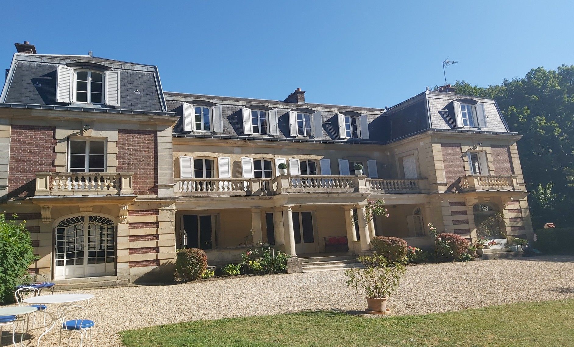 Grand et majestueux manoir français avec façade en pierre et brique, balcon et lucarnes sous un ciel bleu.
