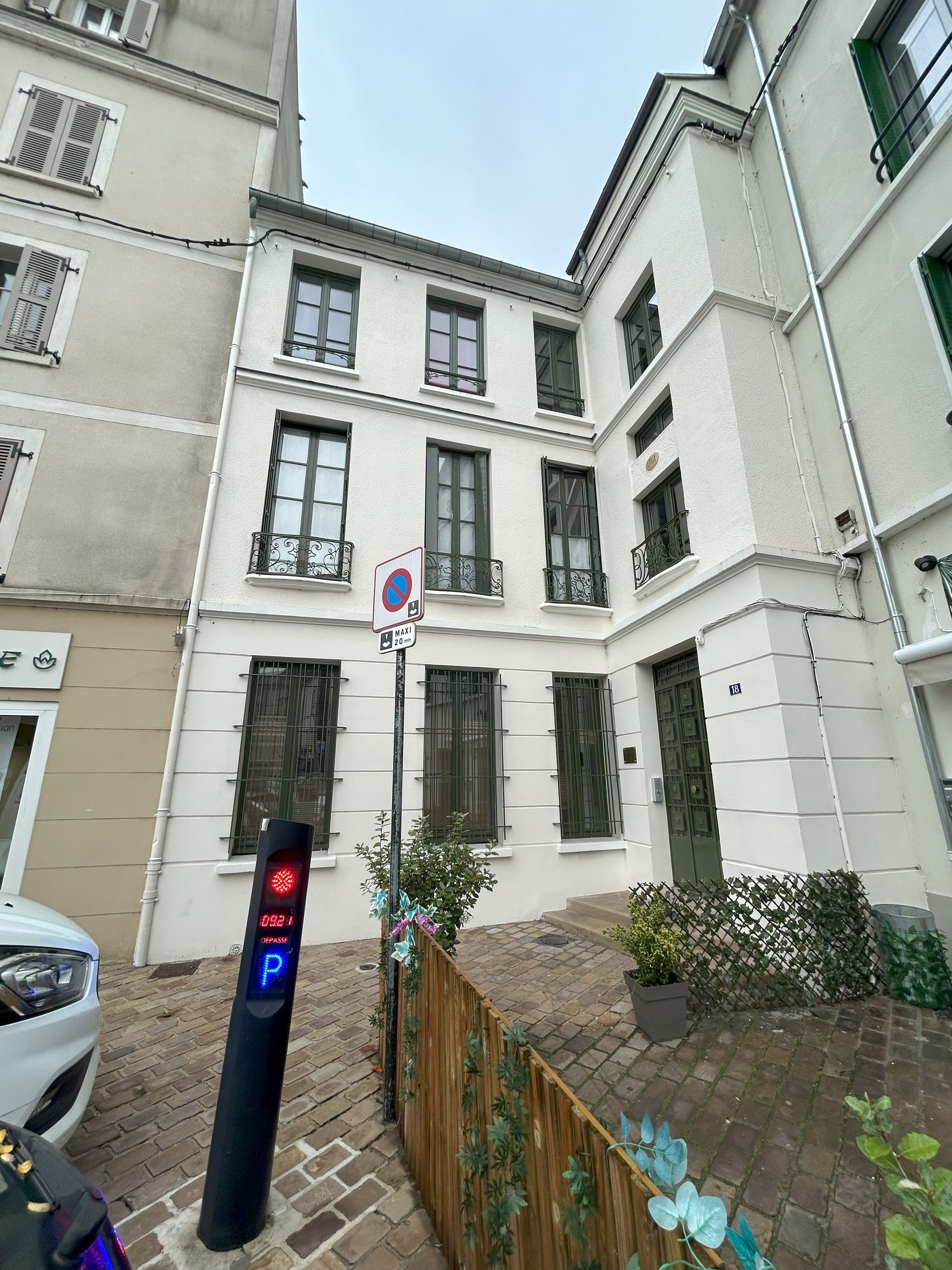 Bâtiment blanc avec volets foncés et panneau de rue.