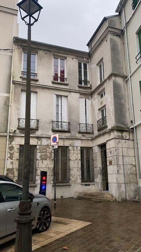 Vieux bâtiment avec façade patinée, lampadaire, voiture et panneau dans une ville européenne.