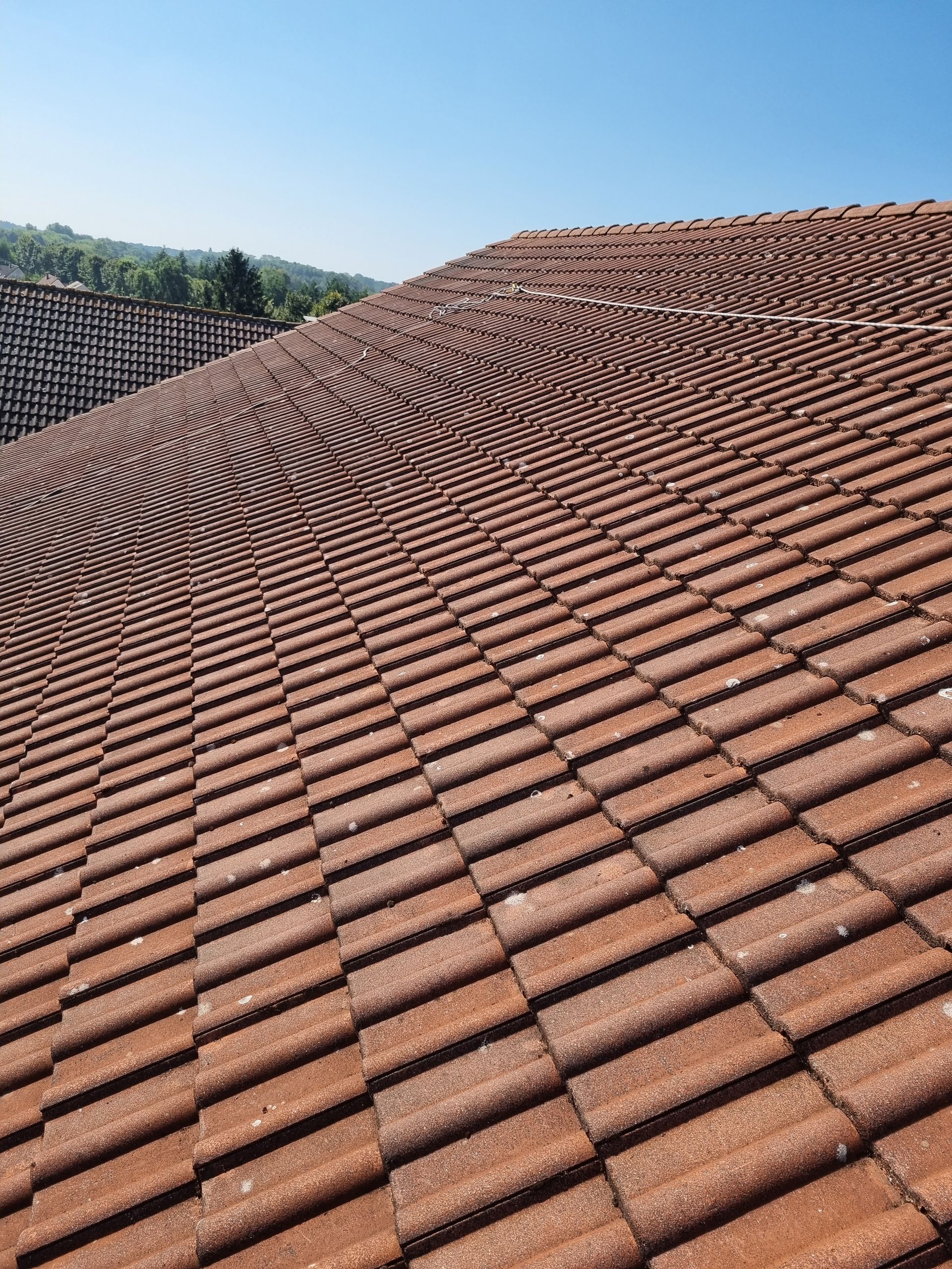 Toit de tuiles rouges sur fond de ciel bleu clair, avec une structure en briques en arrière-plan.