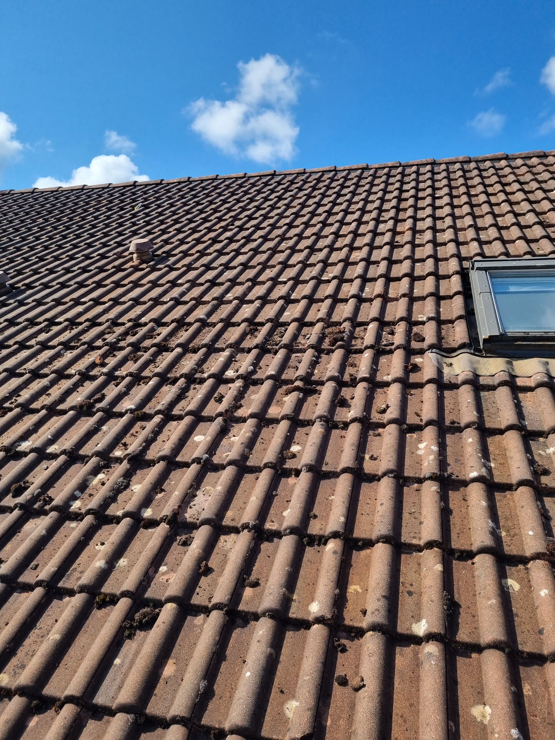 Toit en tuiles brunes avec un puits de lumière sous un ciel bleu avec des nuages.