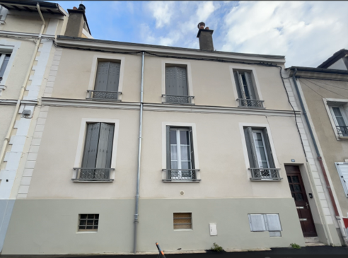 Bâtiment beige de deux étages avec six fenêtres et une porte marron foncé par temps nuageux.