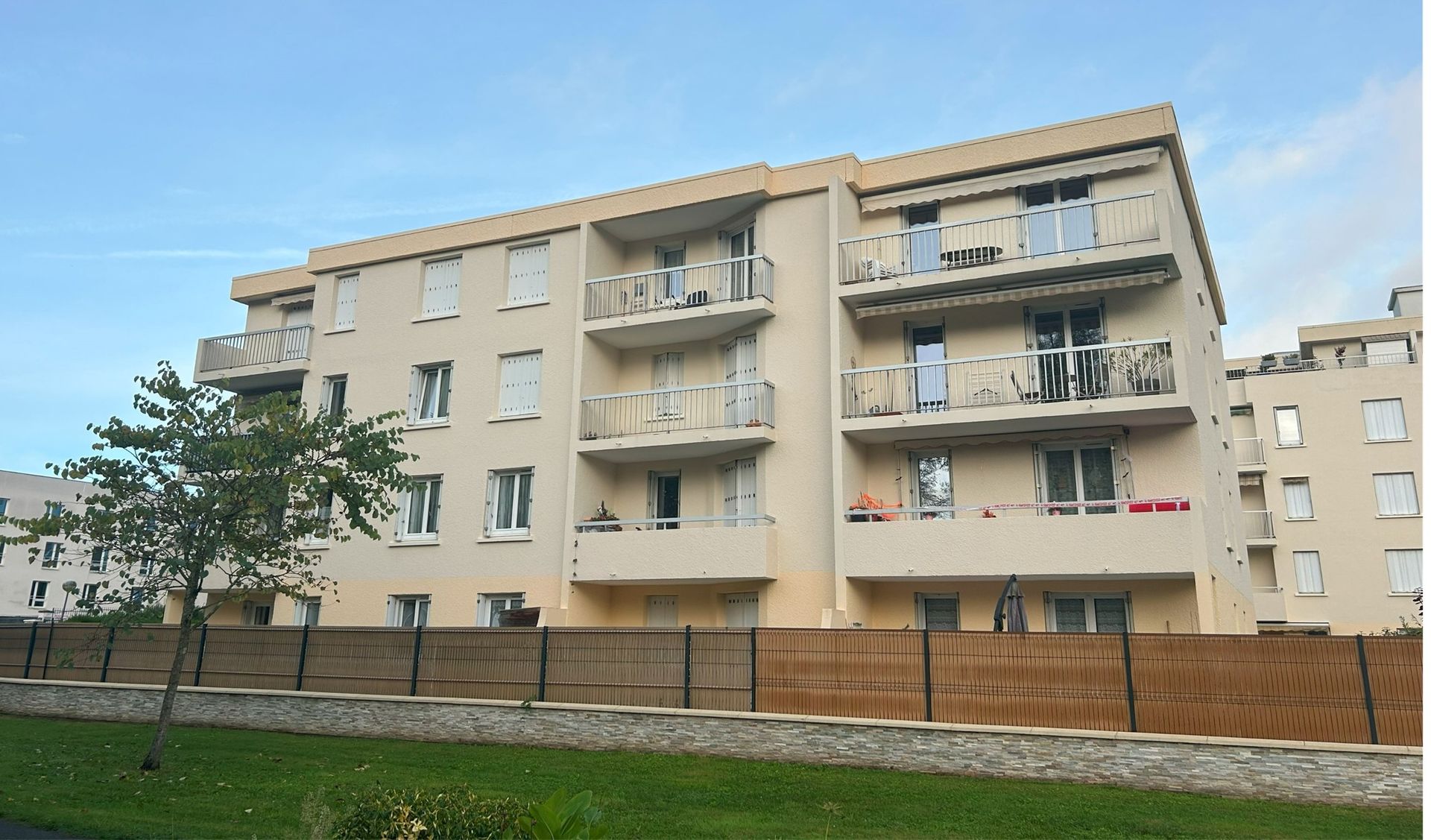 Immeuble d'appartements avec balcons et clôture devant, par une journée ensoleillée.