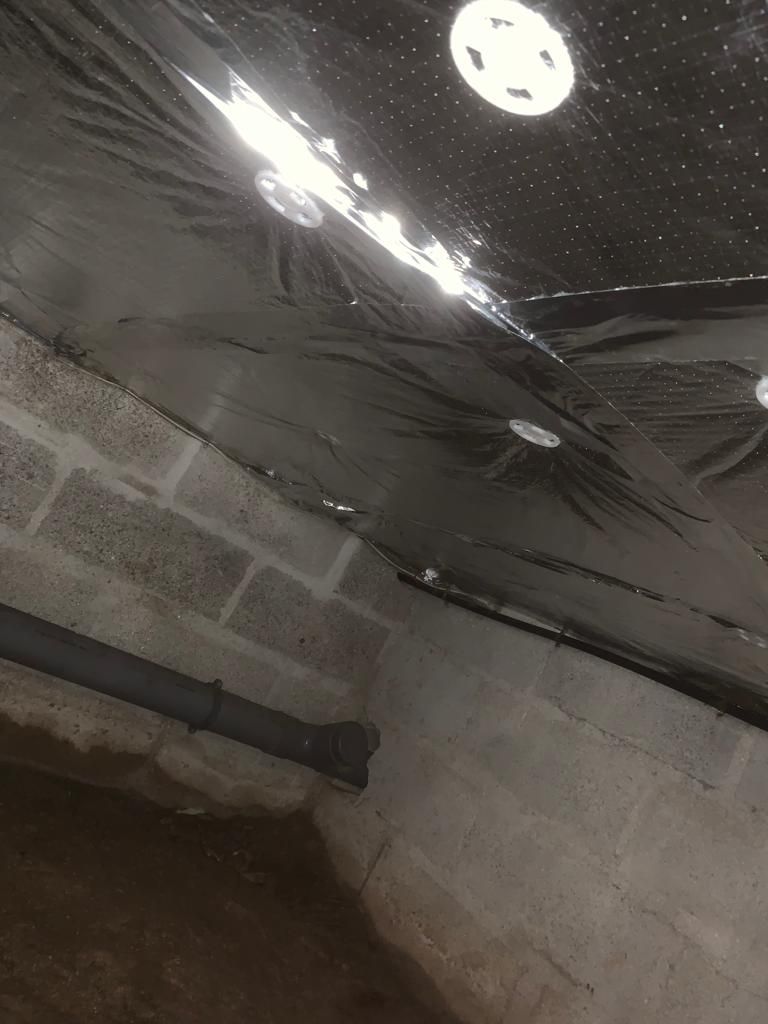 Isolation installée au plafond d'une fondation en blocs de béton; plomberie visible.