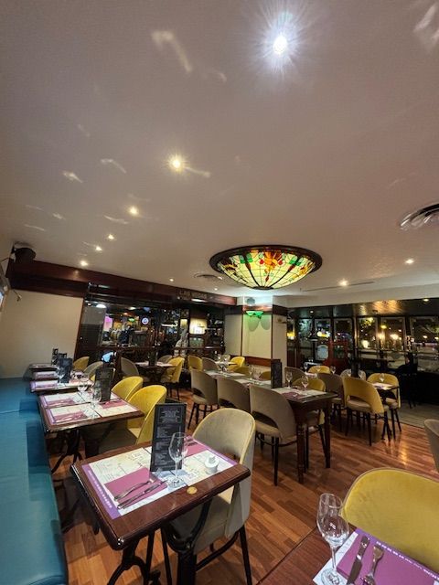 Intérieur de restaurant avec tables dressées pour dîner, chaises jaunes, un plafonnier en vitrail.