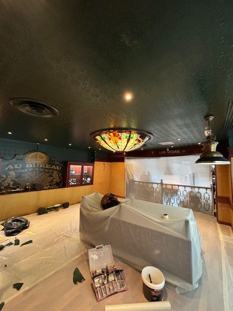 Salle intérieure en cours de rénovation, avec bar couvert, plafond végétalisé et luminaire en vitrail.