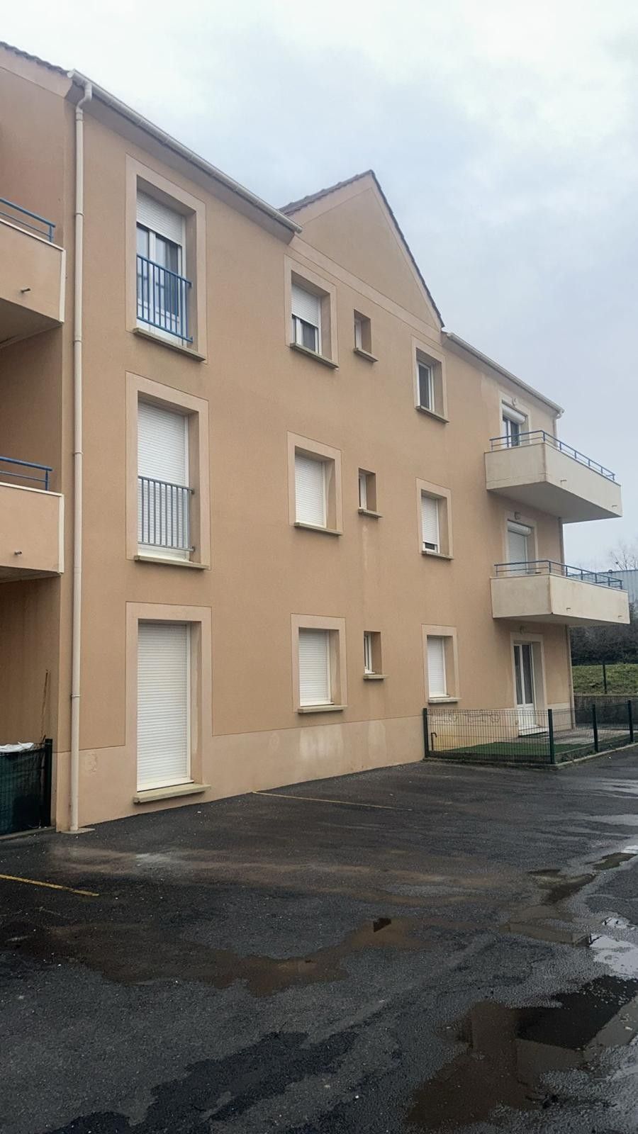 Immeuble d'appartements beige de trois étages avec volets blancs et balcons ; cour pavée.