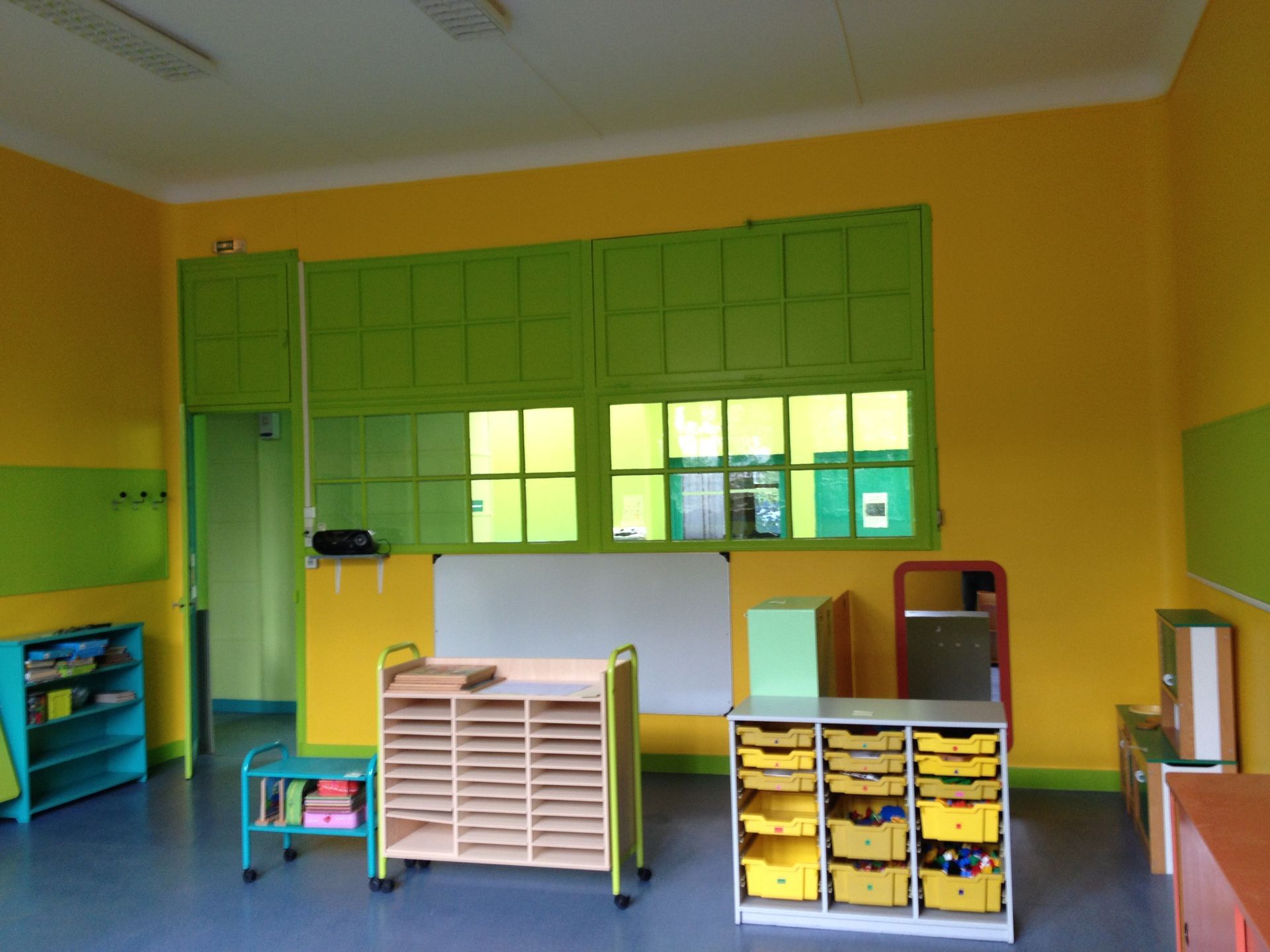 Une salle de classe avec des murs jaunes, des accents verts et diverses unités de rangement.