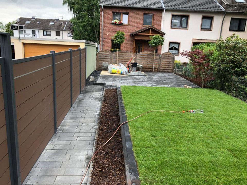 Ein Zaun umgibt einen üppigen grünen Rasen vor einem Haus.