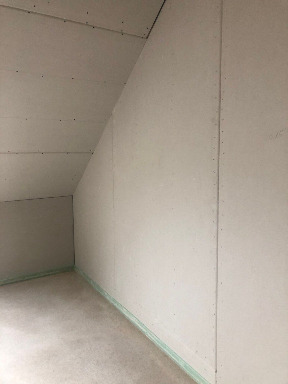 Ein leerer Raum mit schräger Decke und weißer Wand.