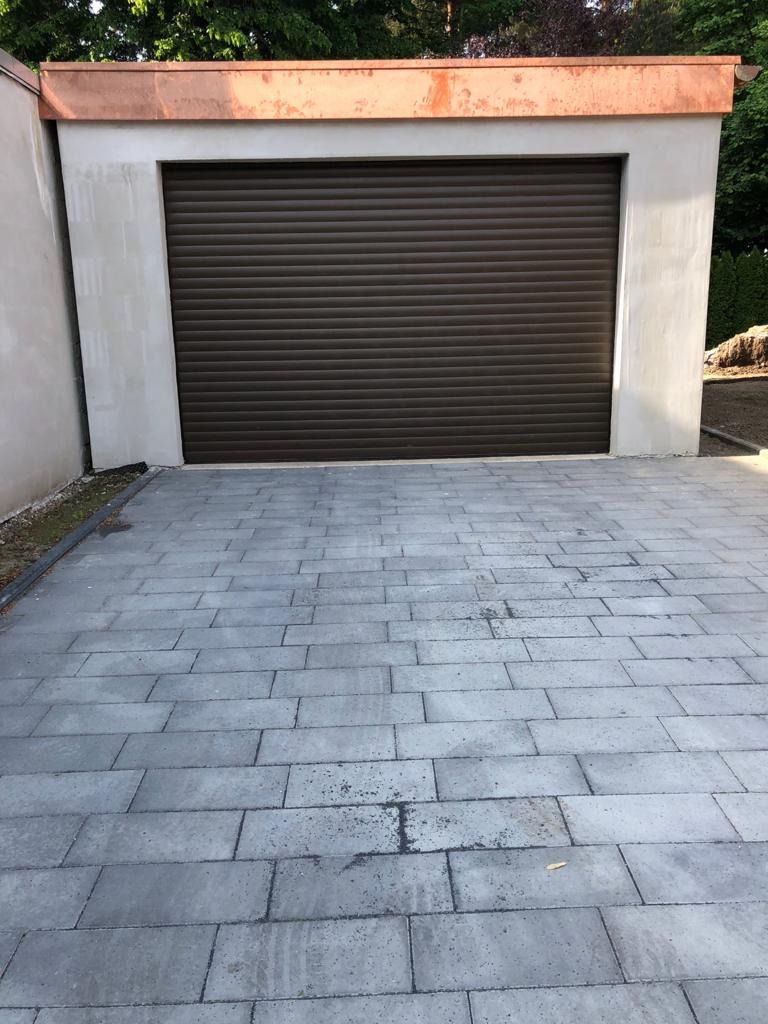 Eine Garage mit einem braunen Garagentor und einer gemauerten Auffahrt