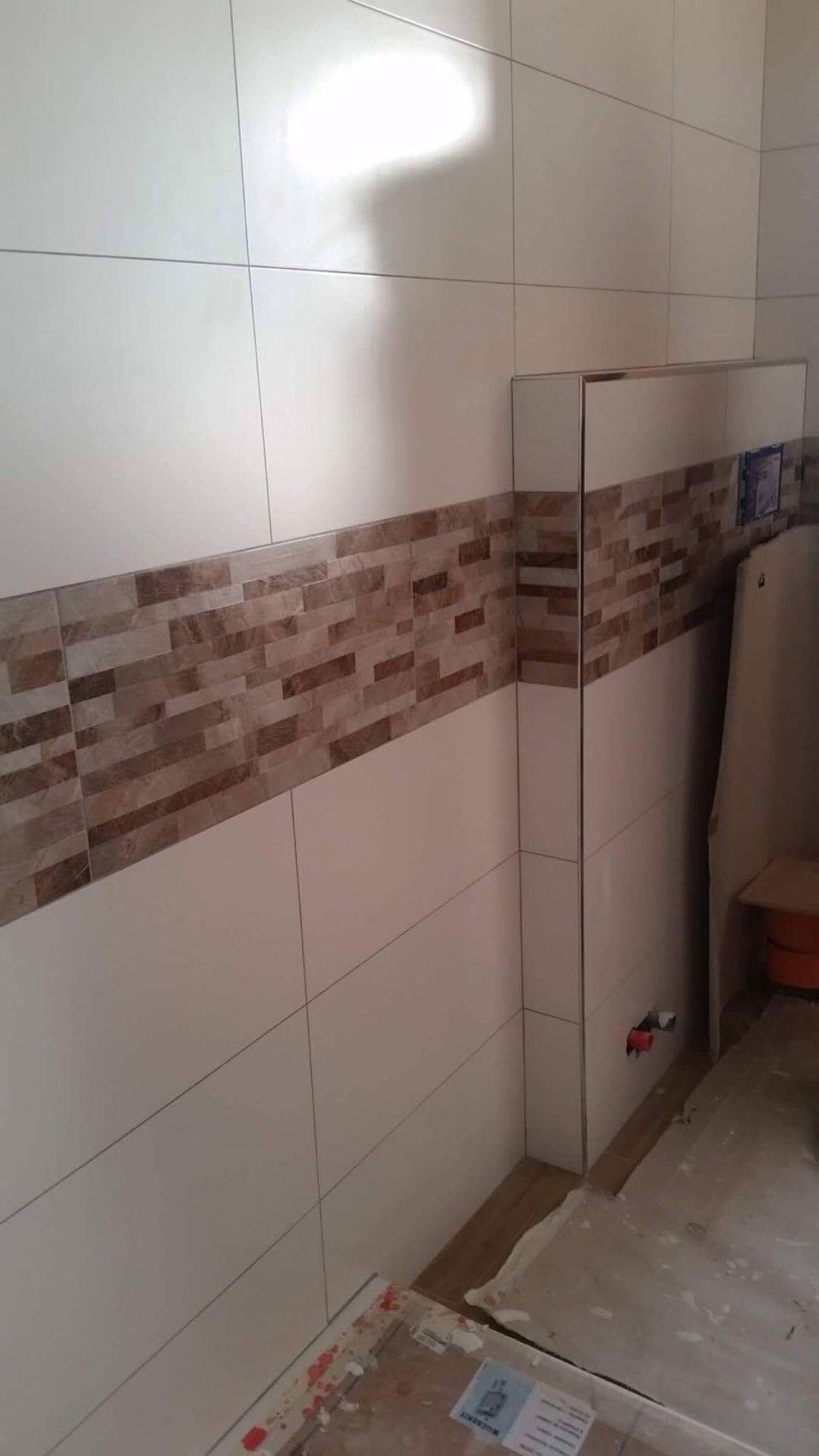 Ein Badezimmer mit weißen Fliesen und braunen Fliesen an der Wand.