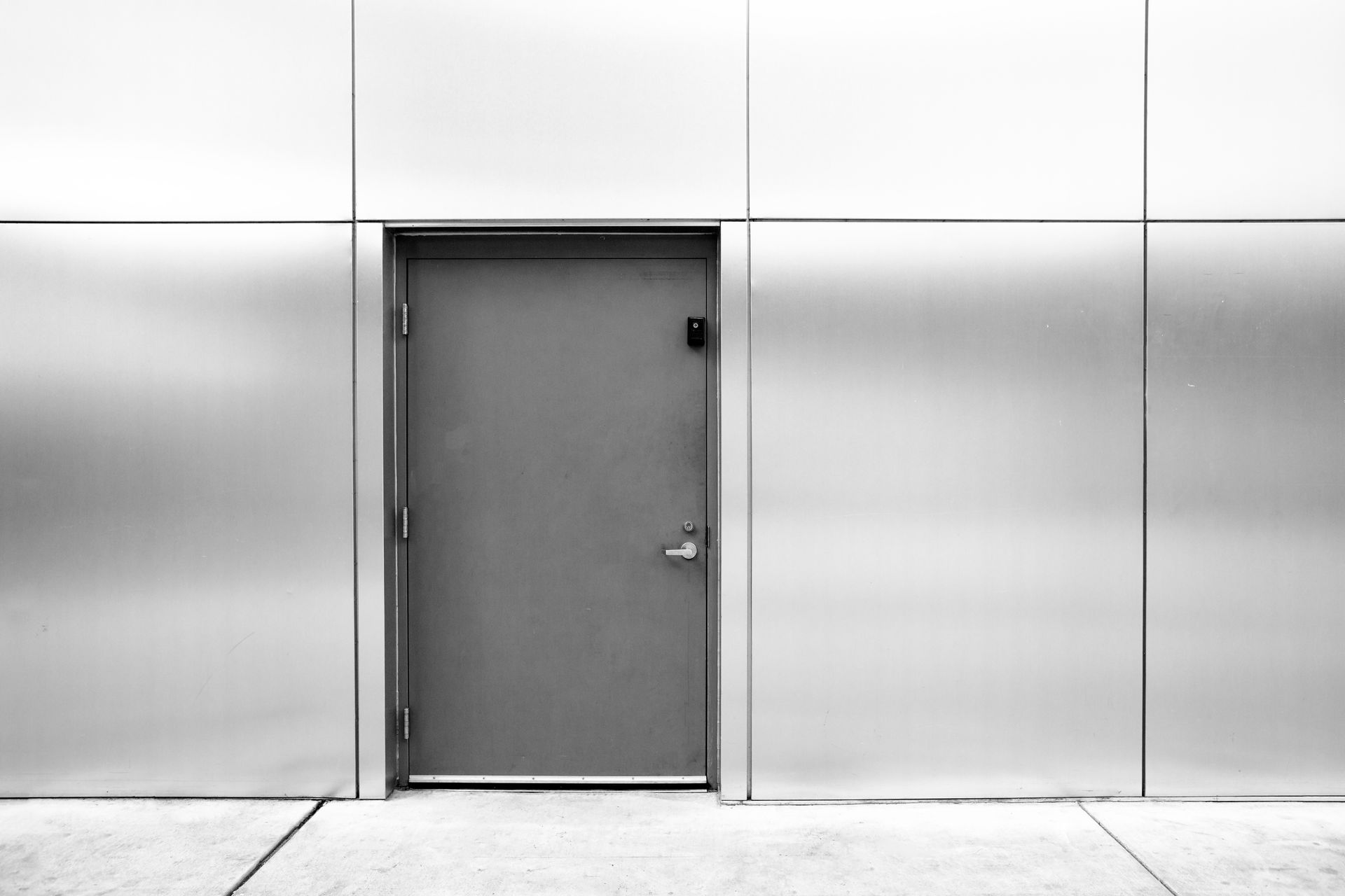 Porte métallique grise encastrée dans un panneau mural argenté, au centre d'un couloir vide de style industriel.