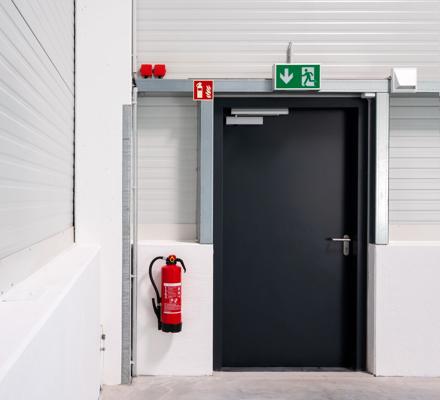 Porte noire dans un couloir blanc avec panneau de sortie et extincteur fixé à côté.