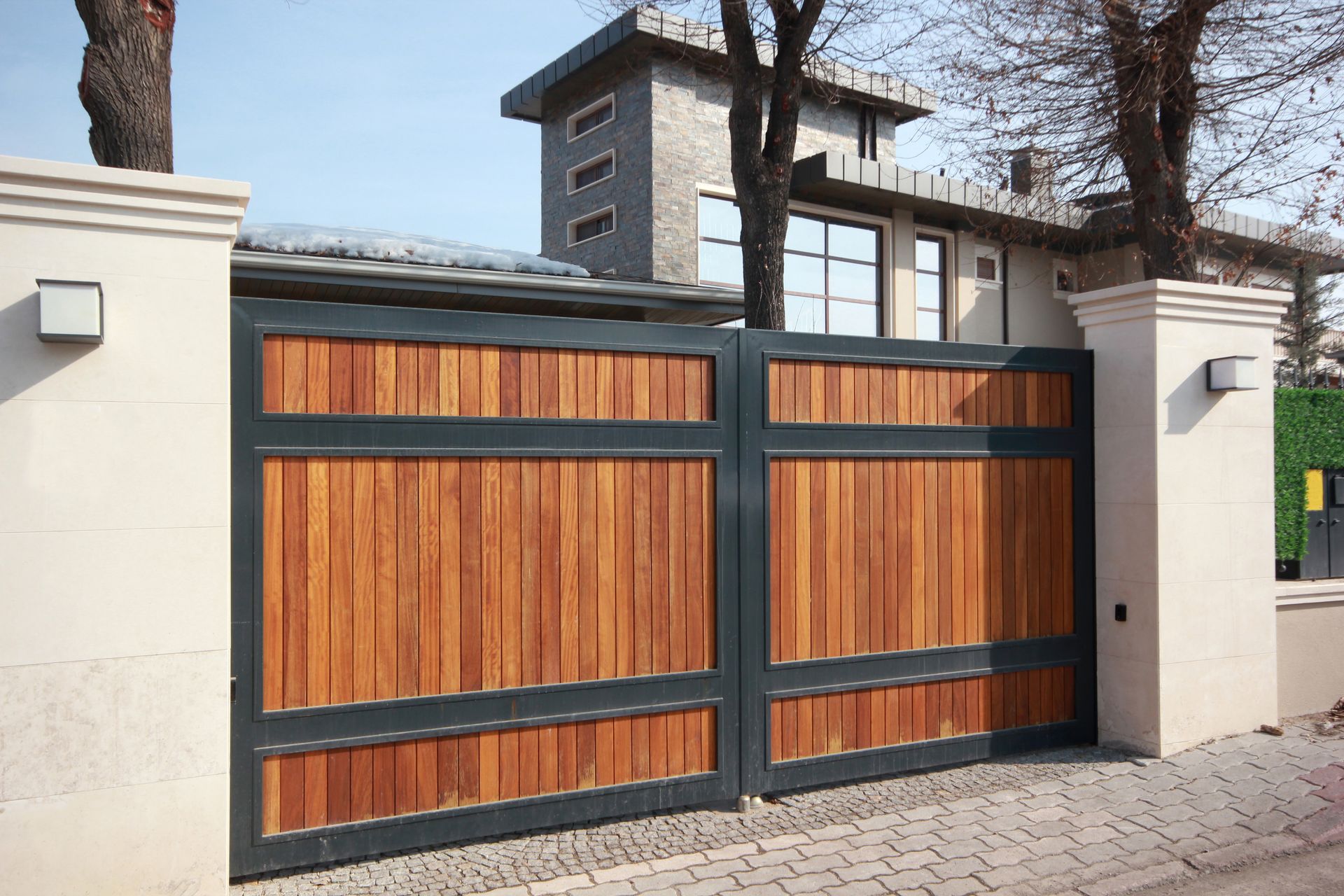 Portail résidentiel contemporain avec panneaux en bois, entre deux piliers maçonnés.
