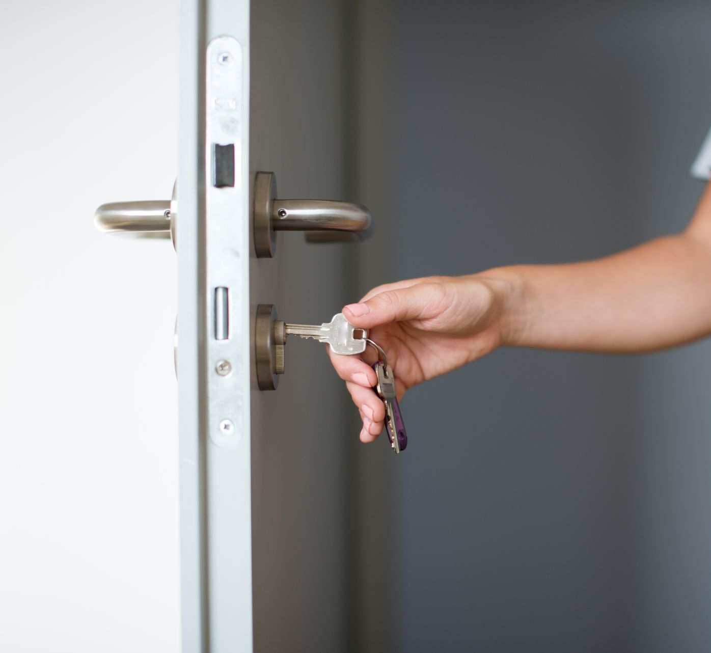 Main tenant une clé pour ouvrir une porte blanche à poignée argentée.