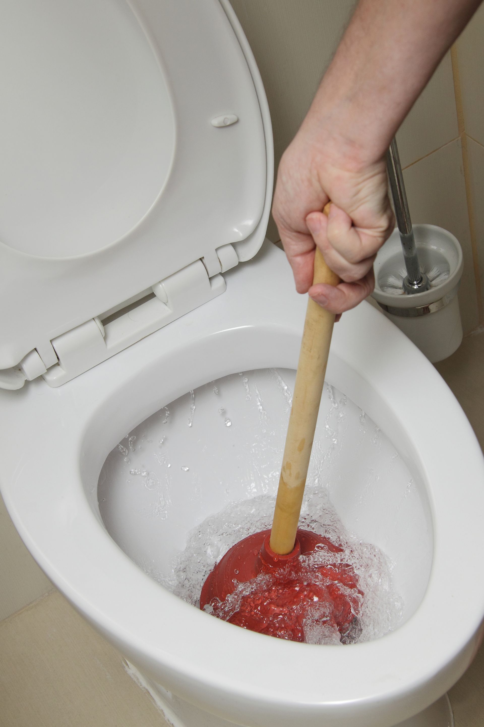 Débouchage manuel des toilettes à l'aide d'un manche en bois, tête de ventouse rouge dans une cuvette blanche.
