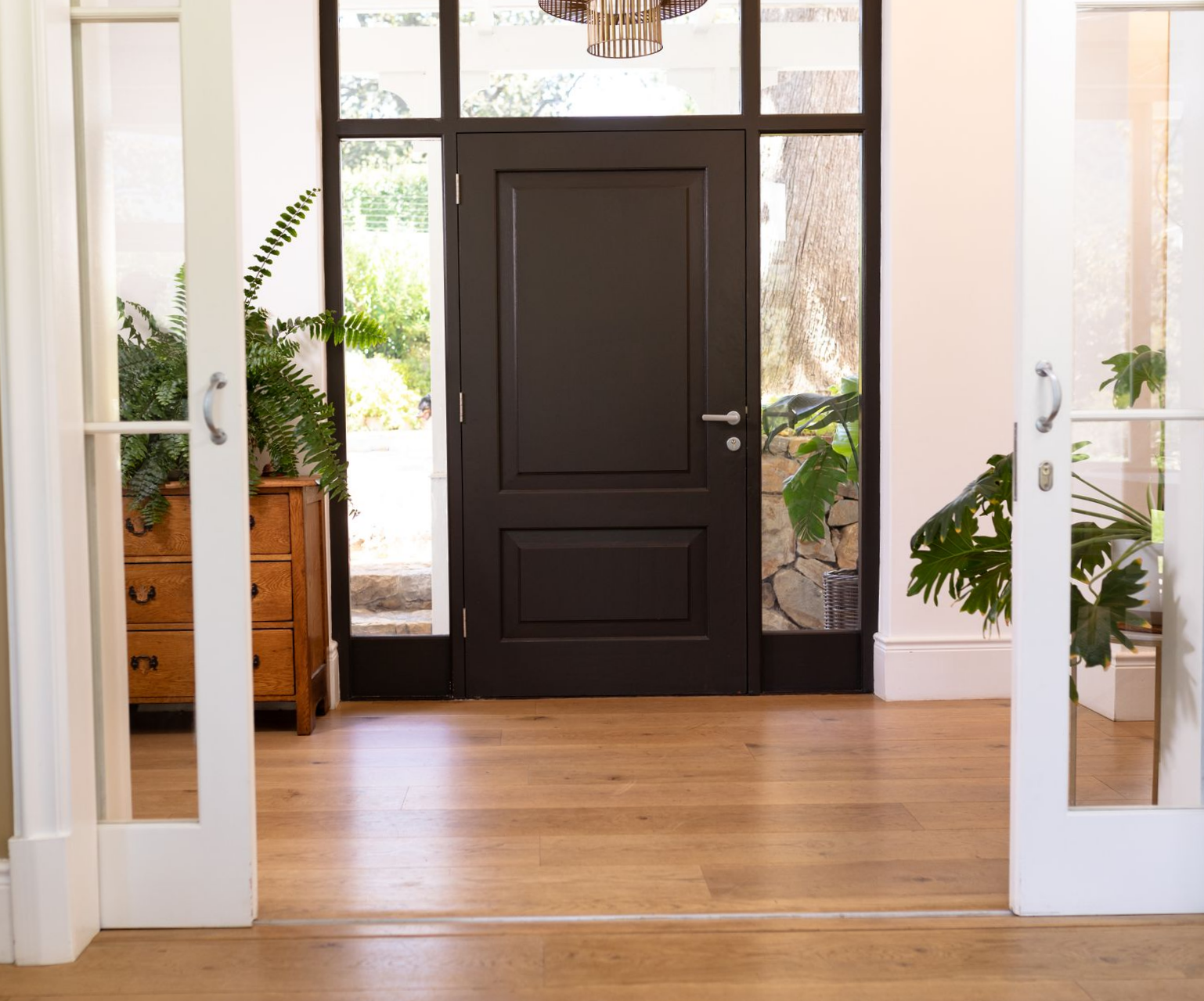 Entrée principale avec porte en bois foncé, parquet et moulures blanches, éclairée par la lumière naturelle.
