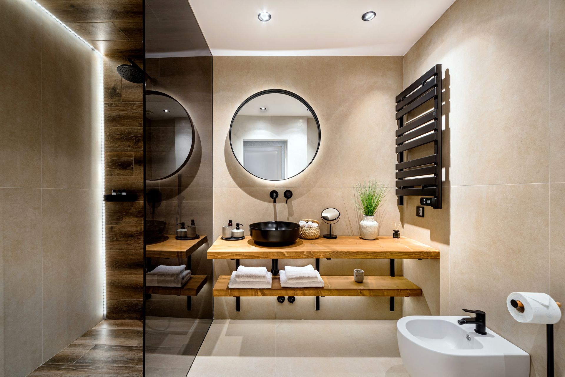 Salle de bains moderne beige avec miroir rond, meuble-lavabo en bois, sèche-serviettes et lavabo blanc
