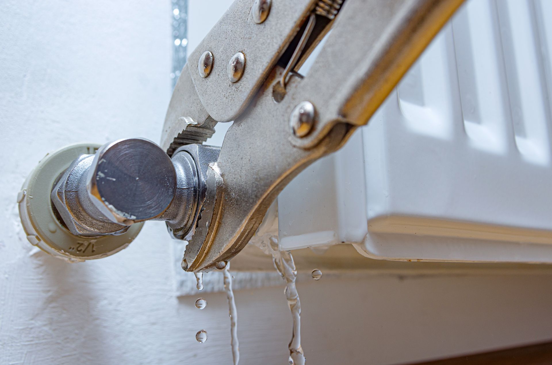 Une pince serre un robinet de radiateur qui fuit, l'eau dégoulinant sur un mur blanc.