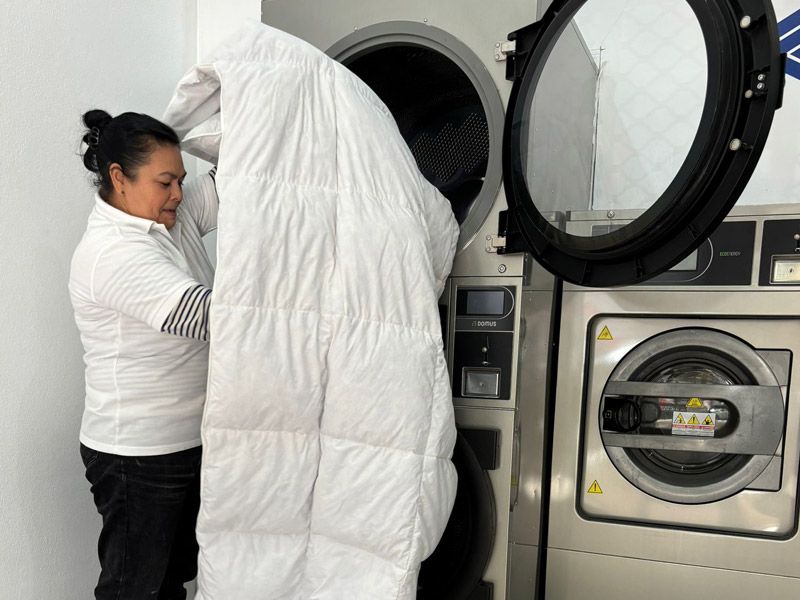 Una mujer está metiendo una manta en una lavadora.