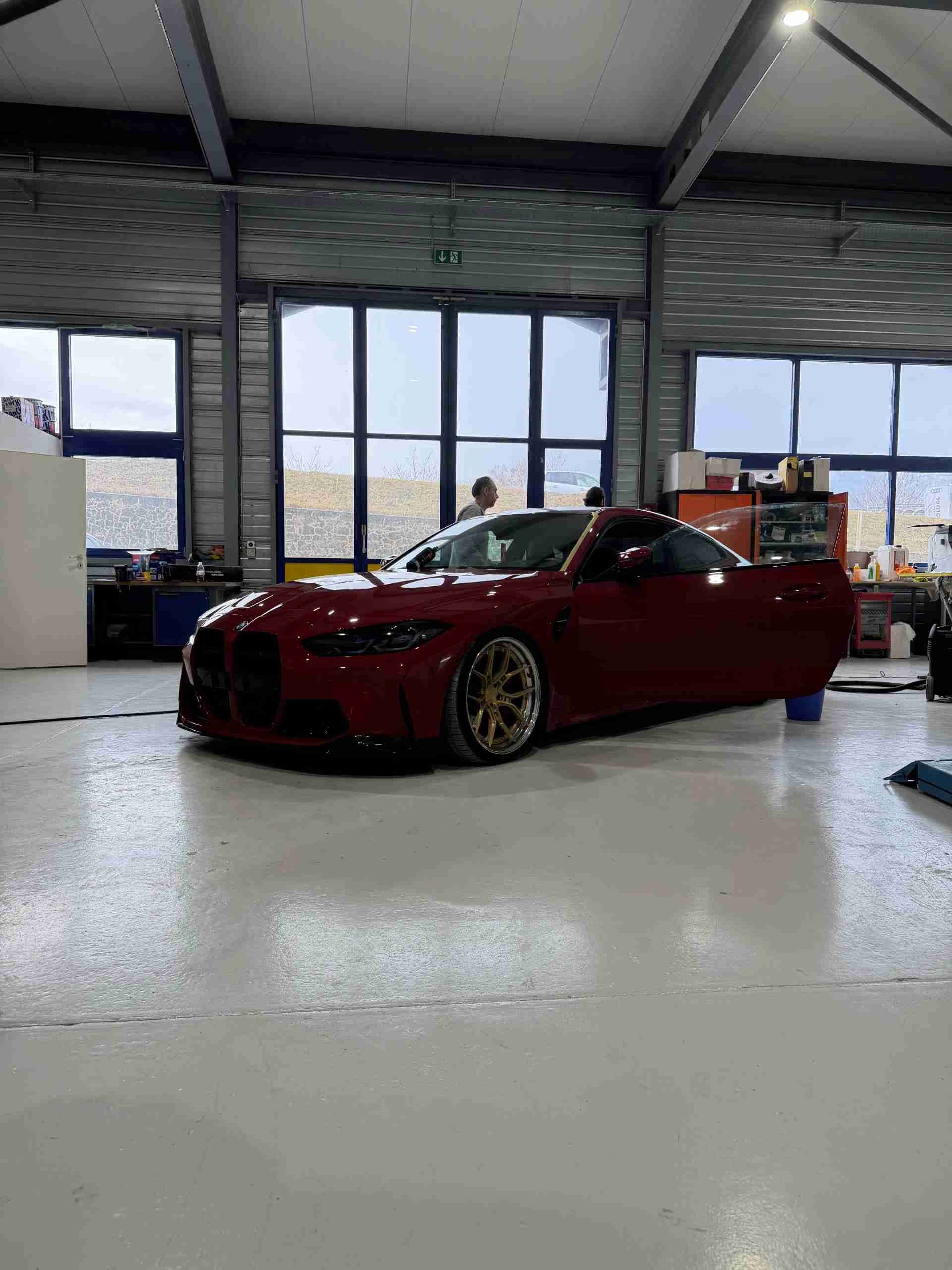 Une BMW M4 rouge avec des jantes dorées garée dans un garage lumineux de style industriel.