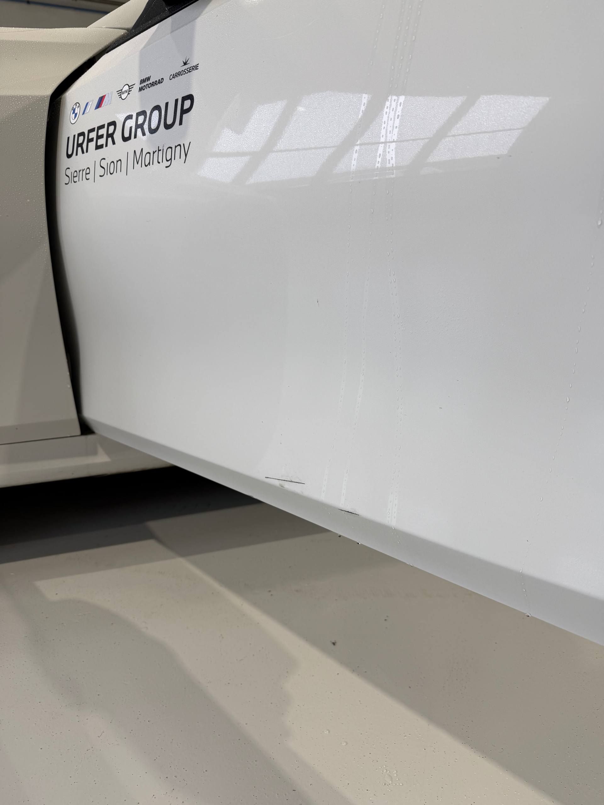 Portière de voiture blanche partiellement ouverte, laissant apparaître le bord avec de petits éclats de peinture