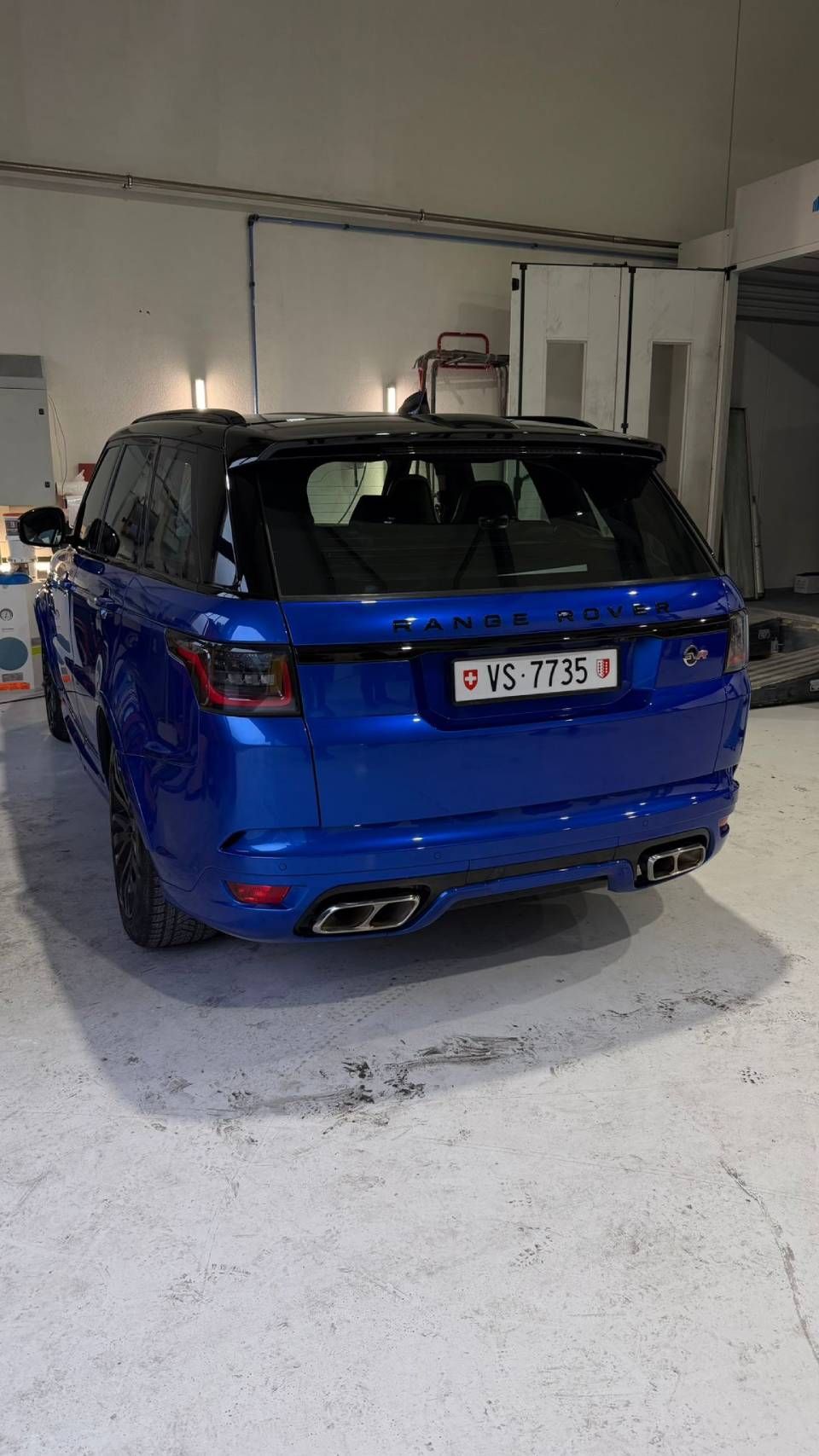 Un Range Rover Sport SUV bleu avec un toit noir, garé dans un garage, vu de l'arrière.