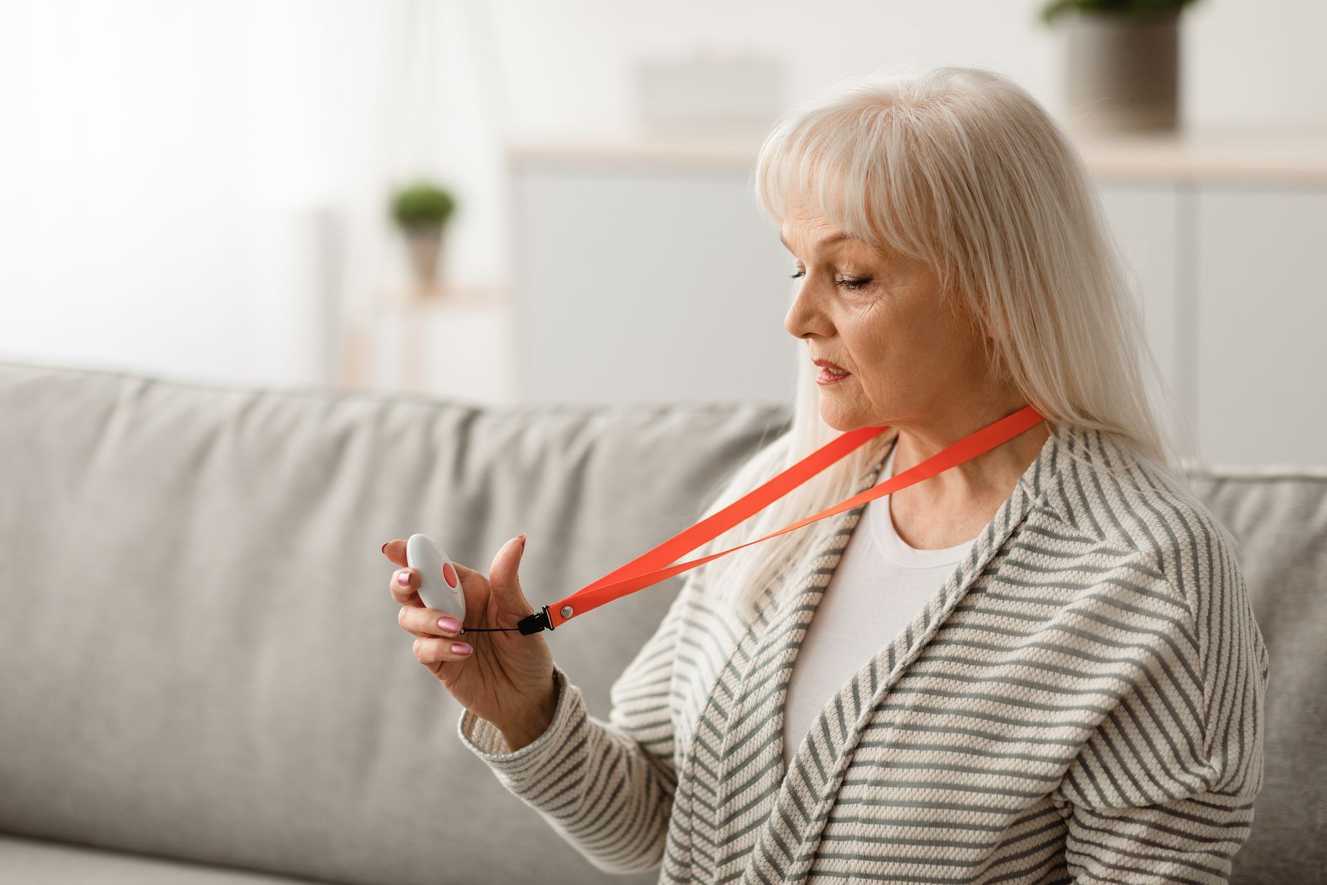 Une femme assise sur un canapé porte un pendentif d'alerte médicale accroché à un cordon rouge.