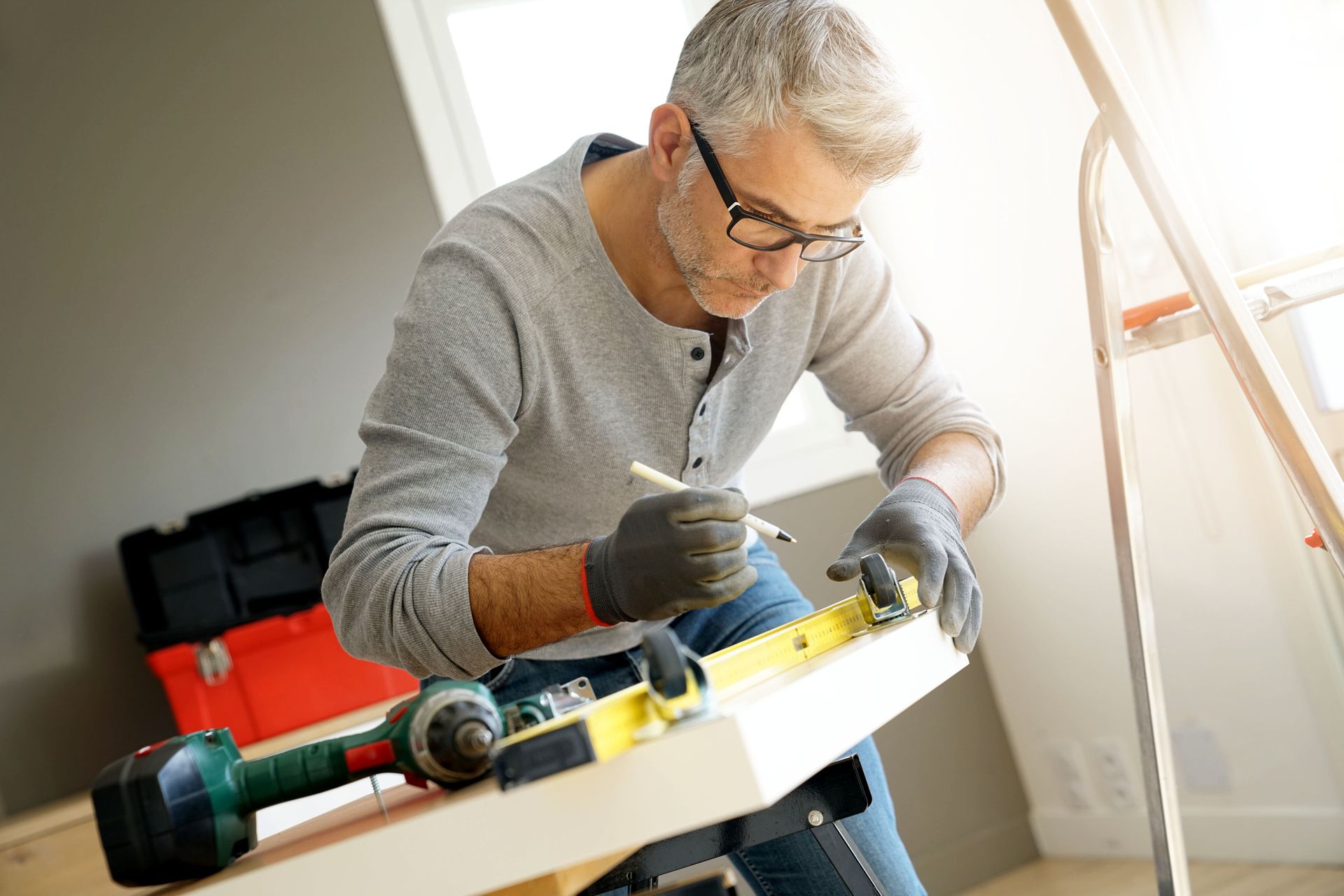 Une personne portant des gants et des lunettes utilise un niveau et un crayon pour mesurer une planche.