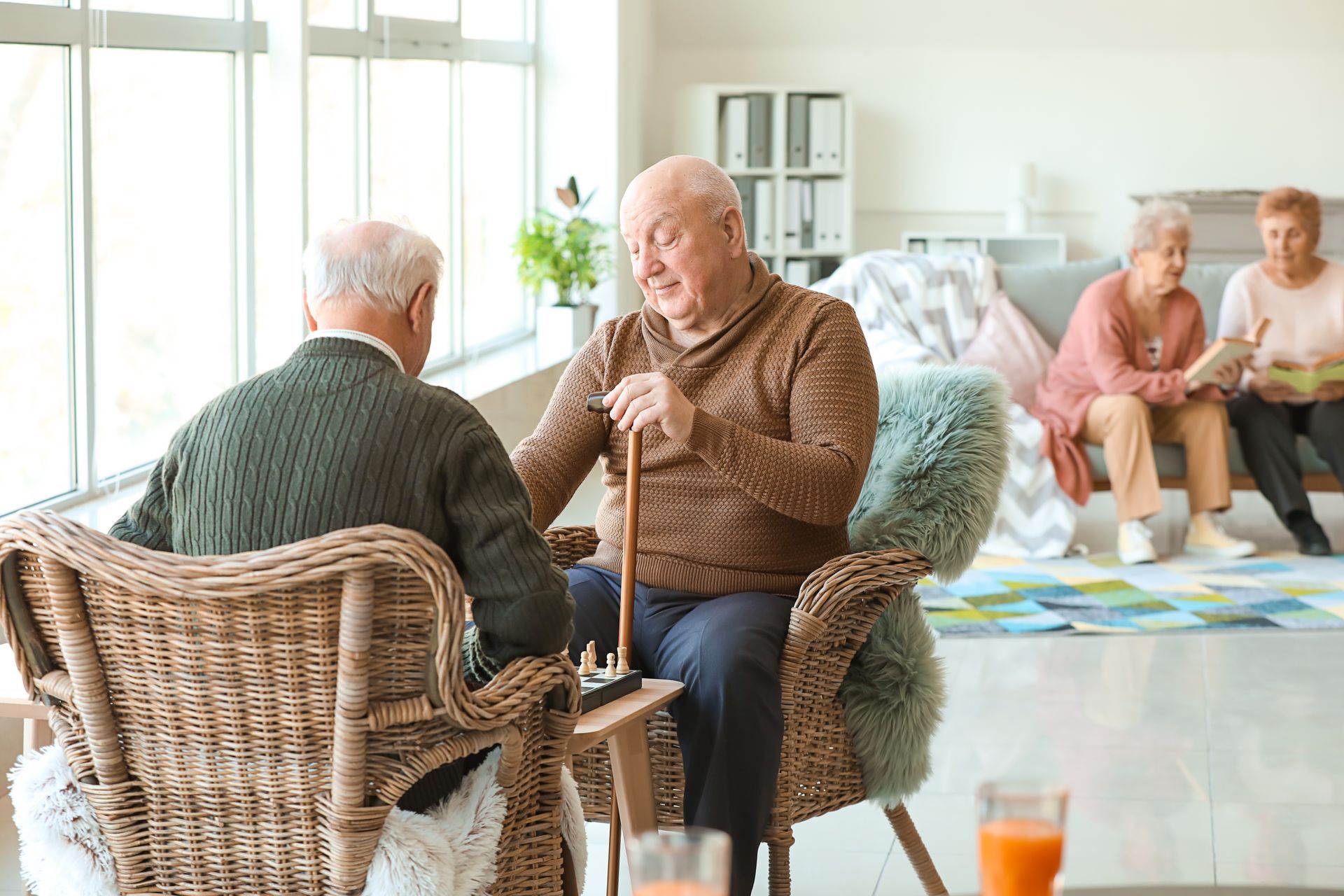 Une personne âgée s'étire à l'intérieur d'une pièce aux tons clairs, avec une plante, une chaise et un lampadaire.
