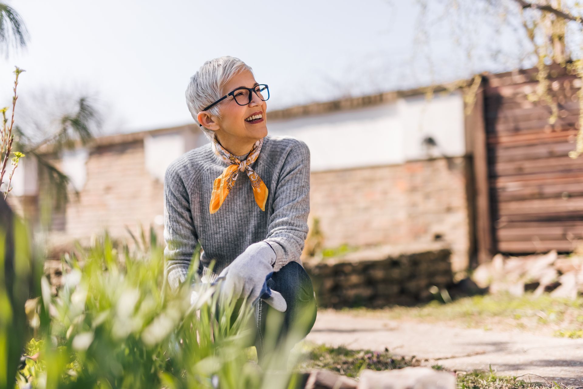 Une femme à lunettes sourit en faisant du jardinage à l'extérieur.