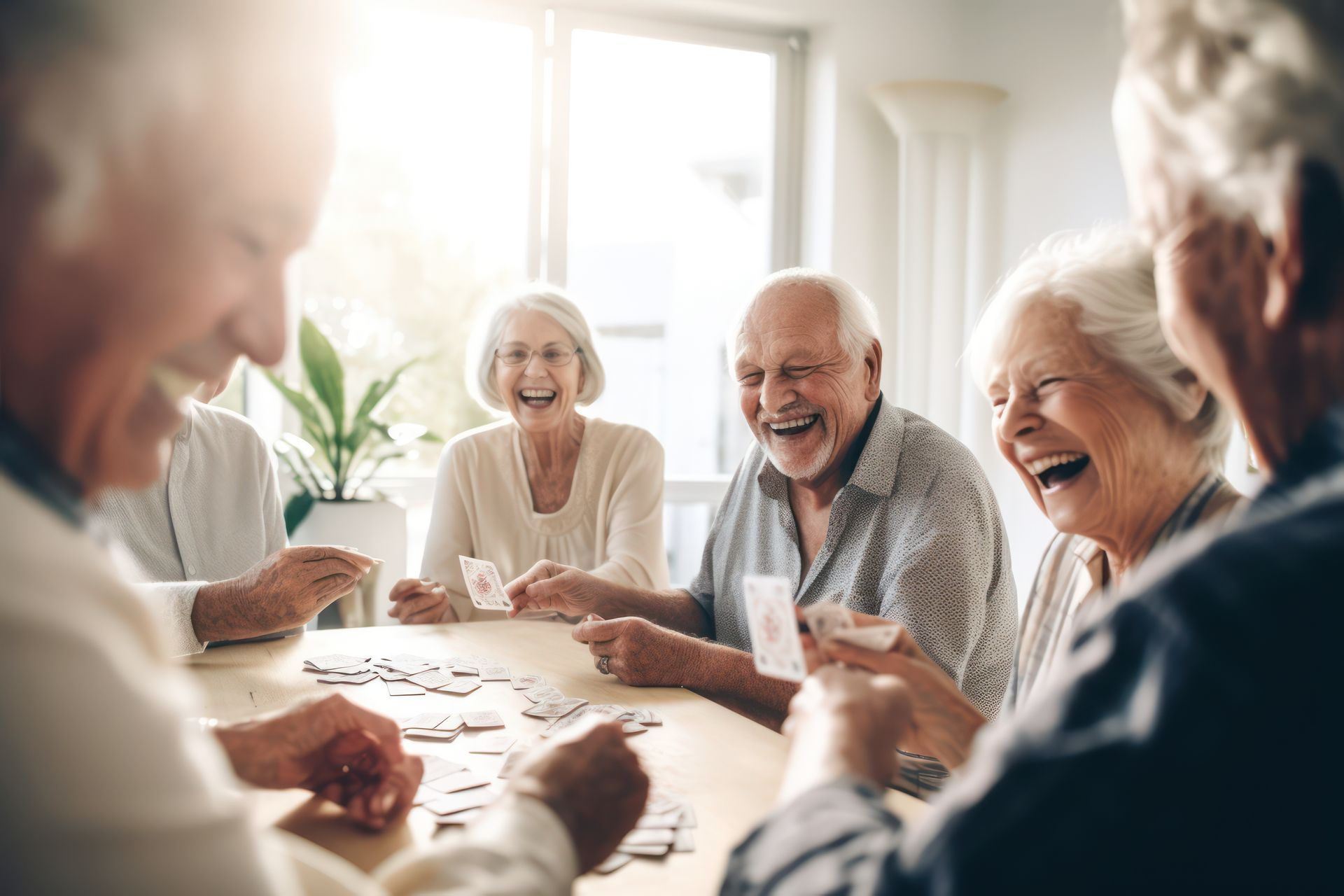 Un groupe de personnes âgées rient et jouent aux cartes autour d'une table à l'intérieur.