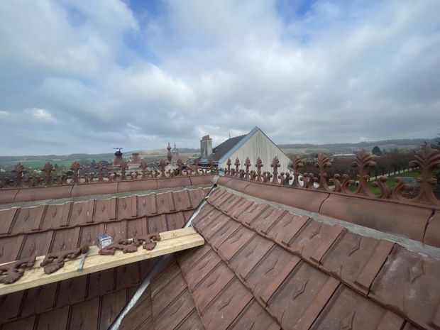 Vue du toit avec des tuiles en terre cuite, des balustrades ornées et un bâtiment triangulaire blanc sous un ciel nuageux